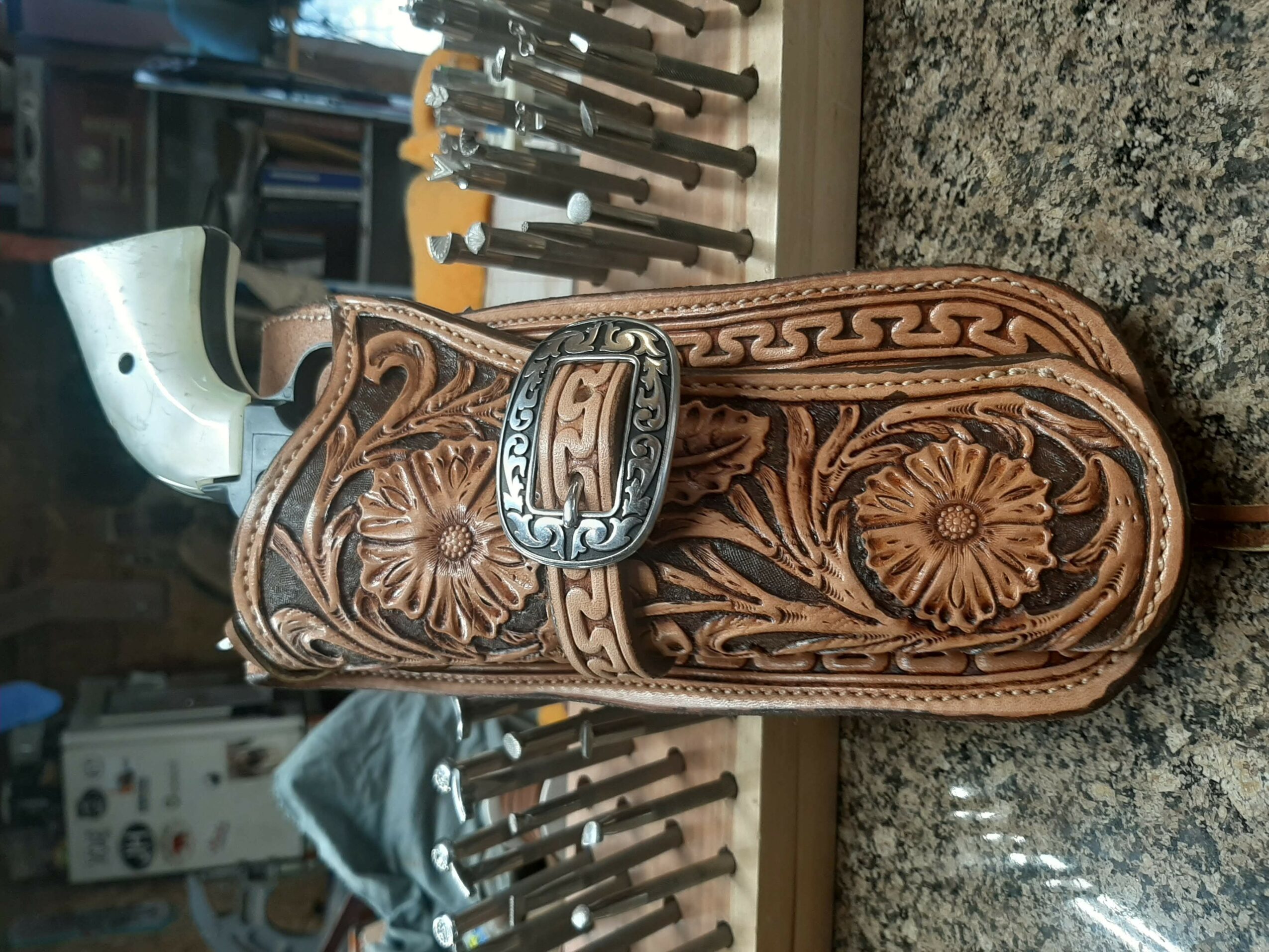 Leather carved belt with floral and geometric patterns, buckle attached, placed on a granite surface.