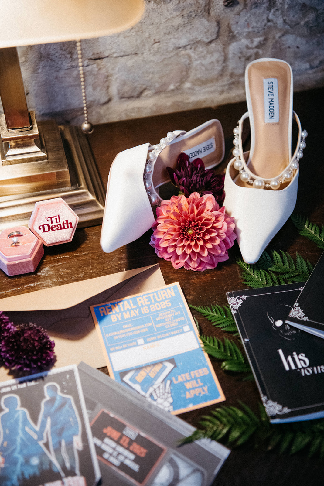 Display of high-heeled shoes with floral decorations, surrounded by cards, a lamp, and decorative items on a table.