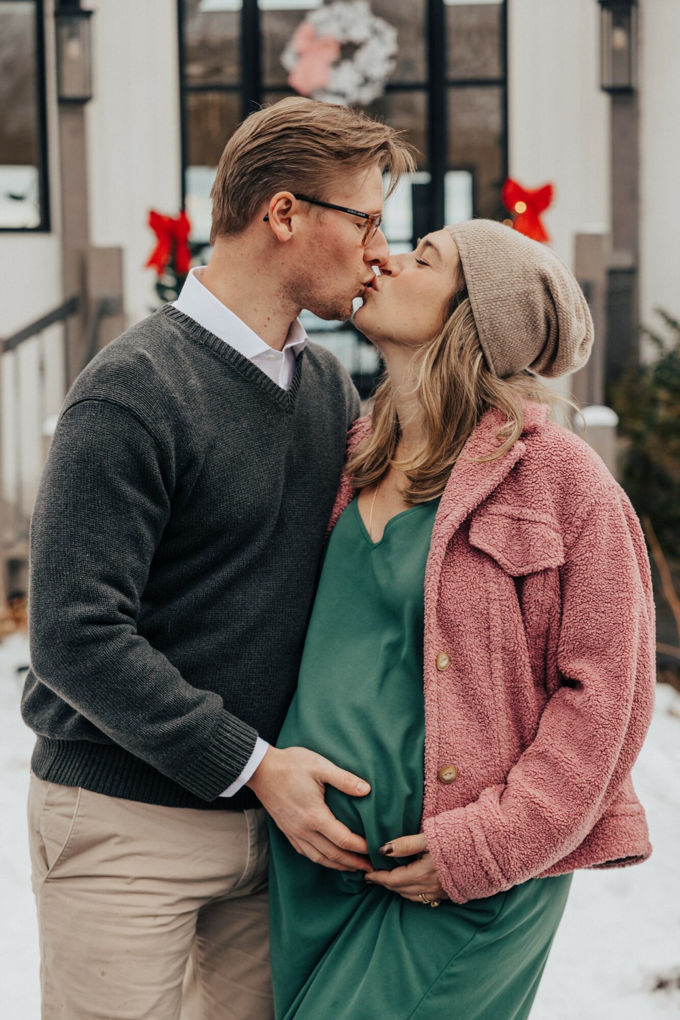 A couple kissing outdoors during winter, with Christmas decorations in the background, both wearing warm clothing.