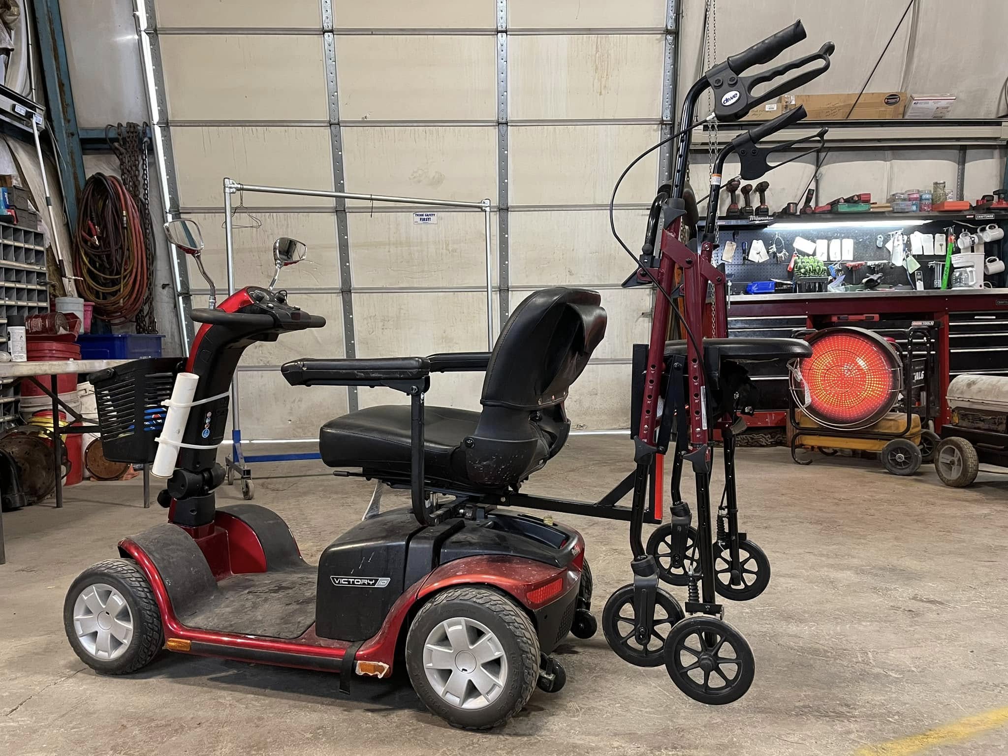 Mobility scooter with a seat, handlebars, and a basket, parked inside a garage with tools and equipment in the background.