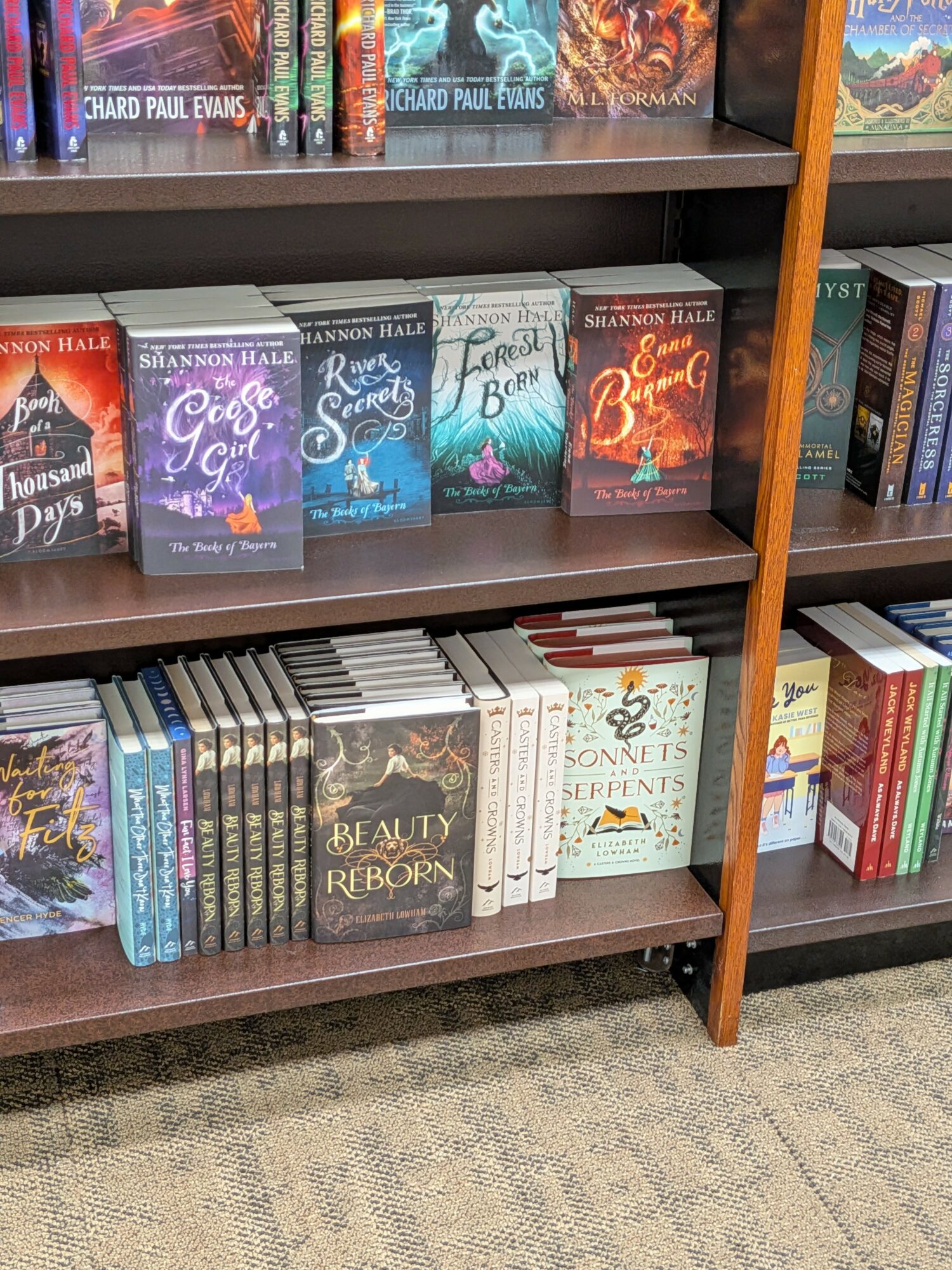 Books on a bookshelf, including titles like 'Beauty and the Reborn' and 'Songs of the Seventy-Sixth,' arranged on shelves.