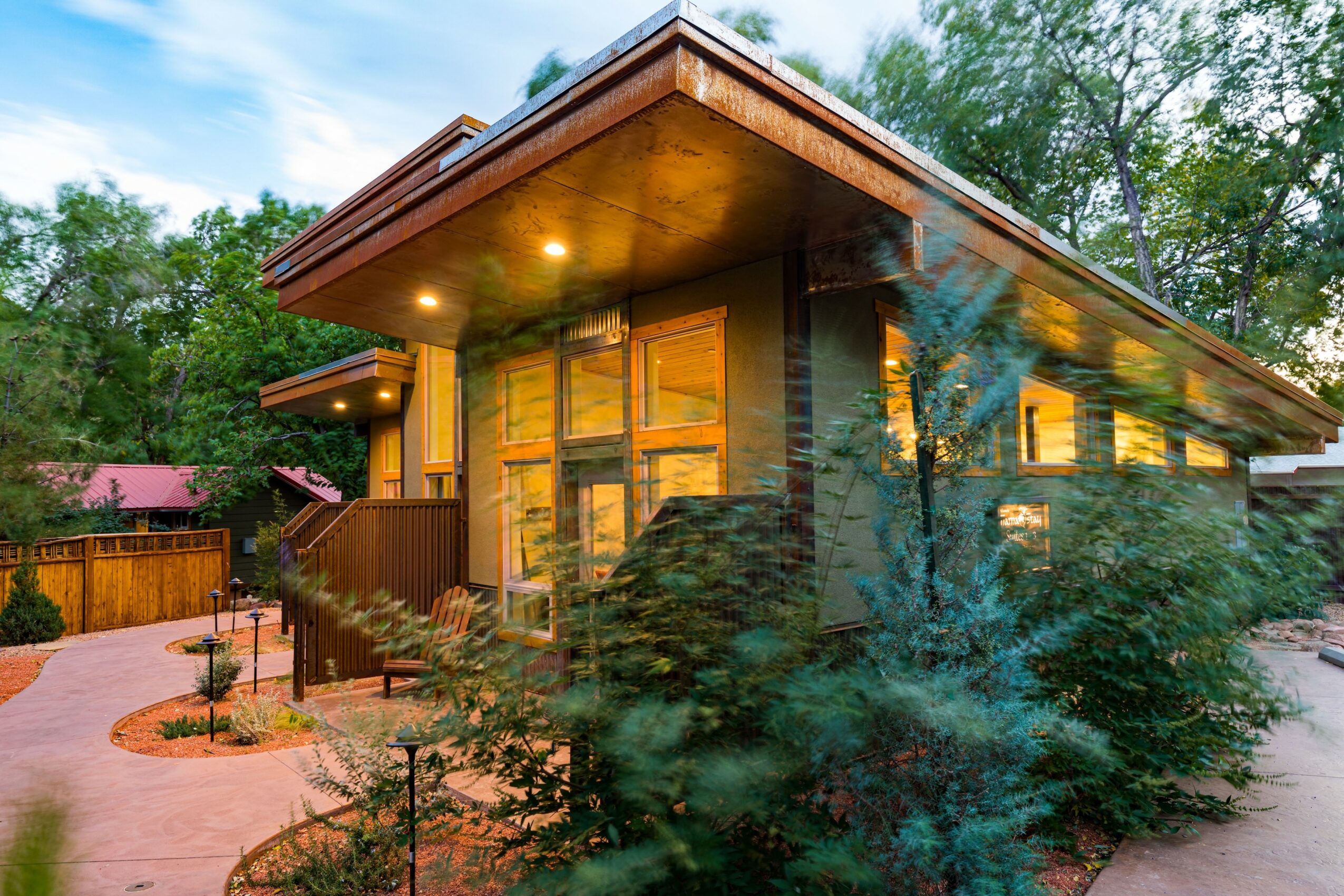 Modern house with large windows, surrounded by trees and a landscaped yard, during daytime with blue sky.
