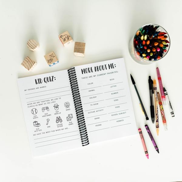 Open activity book with quiz questions, wooden blocks, colored markers, and a cup of colored pencils on a white surface.