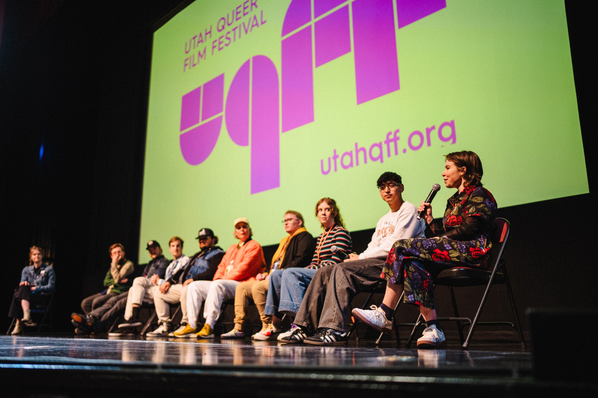 Eight people sit on stage in front of a large screen displaying 'Utah Queer Film Festival' and 'utahaff.org' in pink and purple text.
