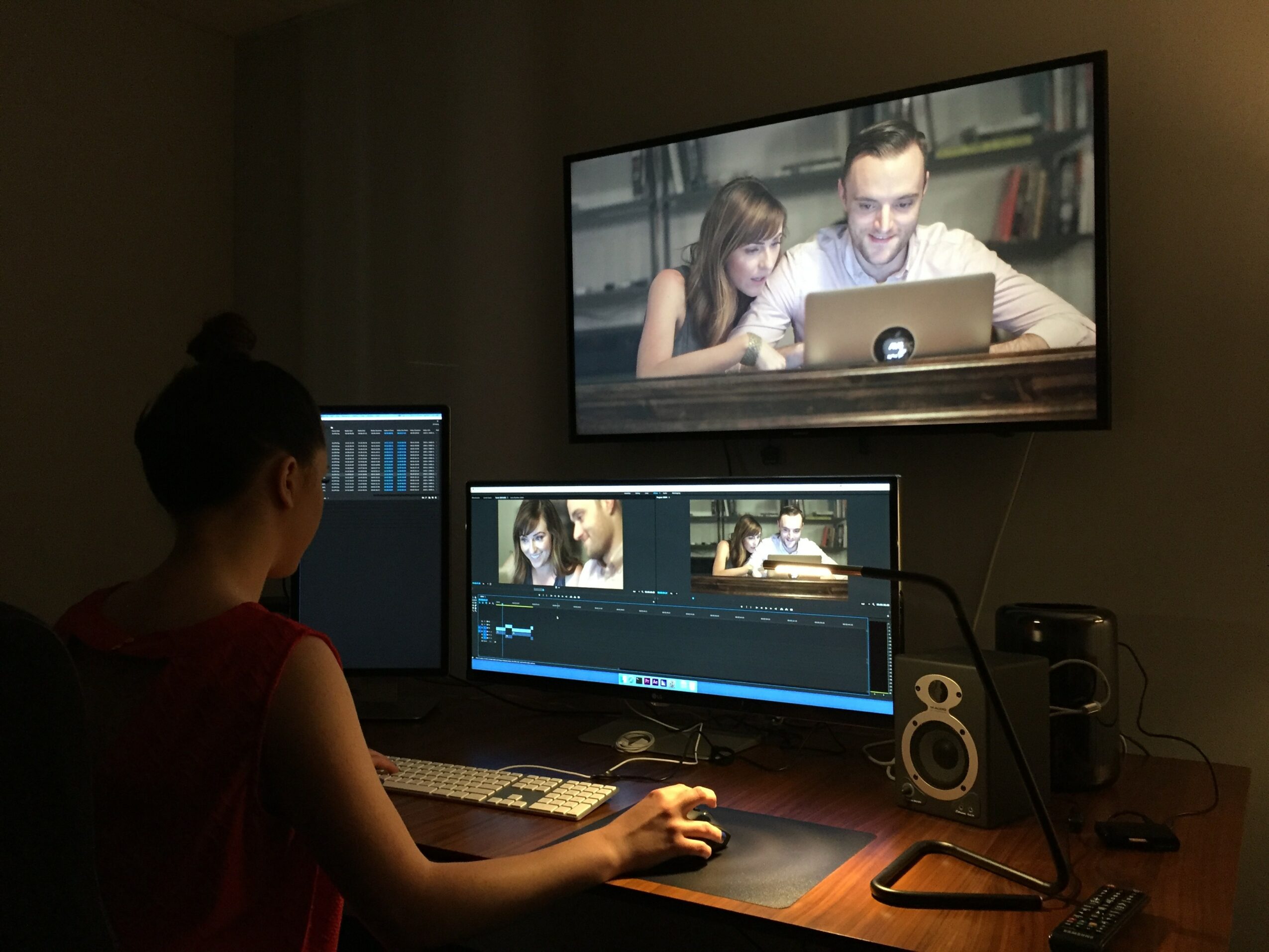 Person working on a computer with two monitors, one showing a video call with a man and a girl, in a dimly lit room.
