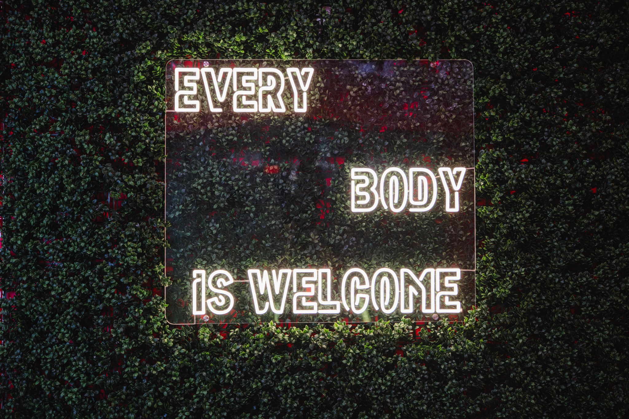 A sign with the message 'Every body is welcome' in white letters on a dark background, surrounded by colorful speckles.