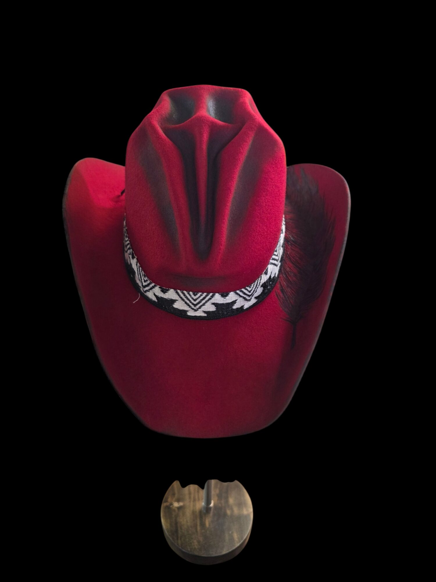 Red cowboy hat with black and white band, viewed from above, on a black background.