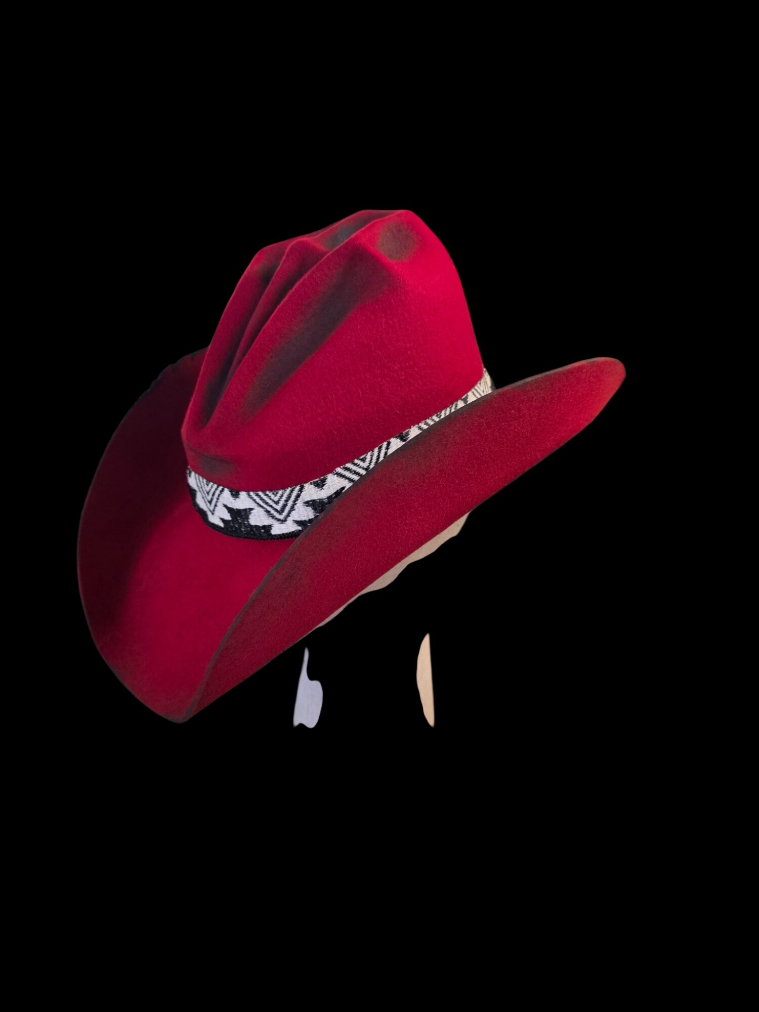 Red cowboy hat with a patterned band, isolated on a black background.