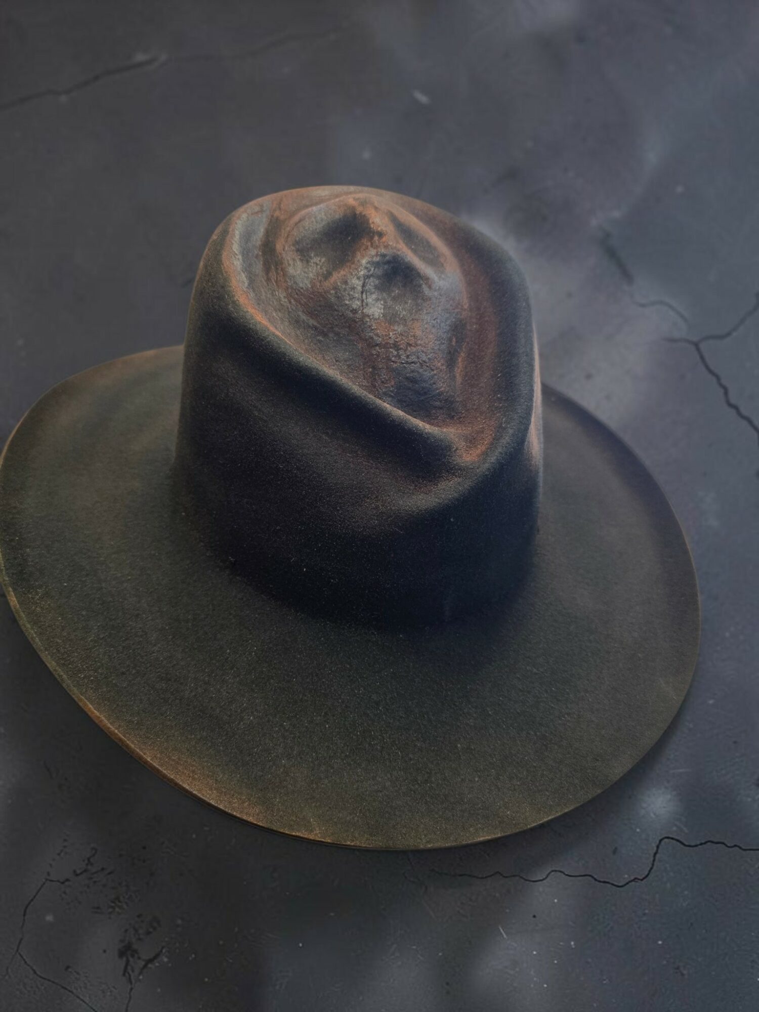 A black wide-brimmed hat with a rounded crown, placed on a dark cracked surface.