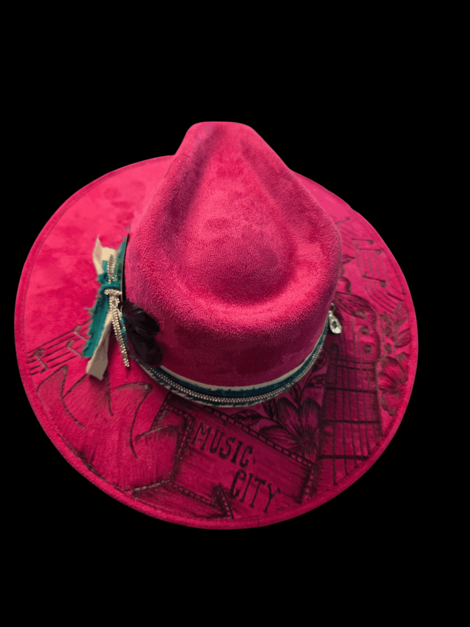 Pink hat with a wide brim, decorated with a clothespin and a small charm, against a black background.
