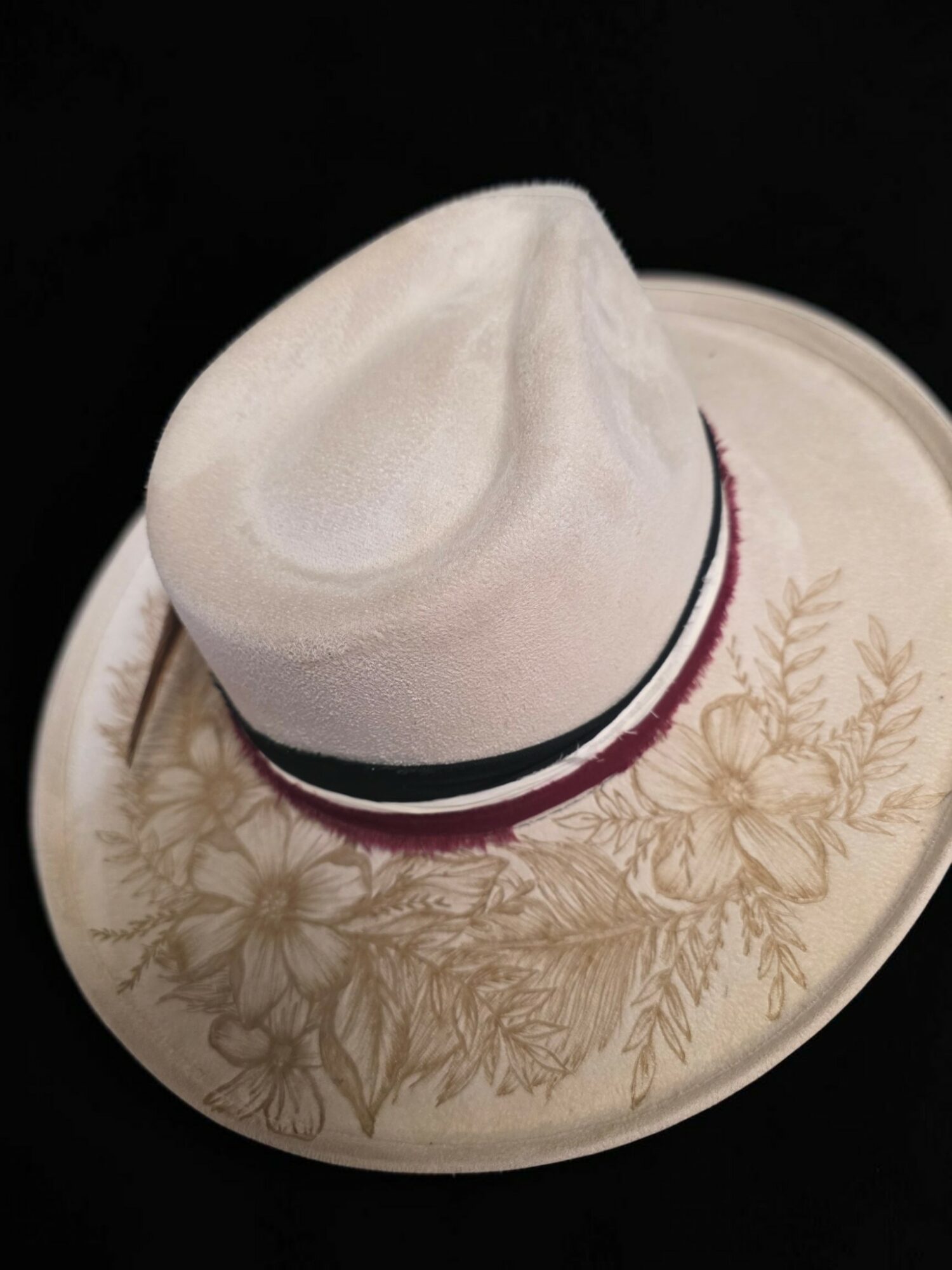 White hat with a black and red band resting on a decorative plate with floral design, against a black background.