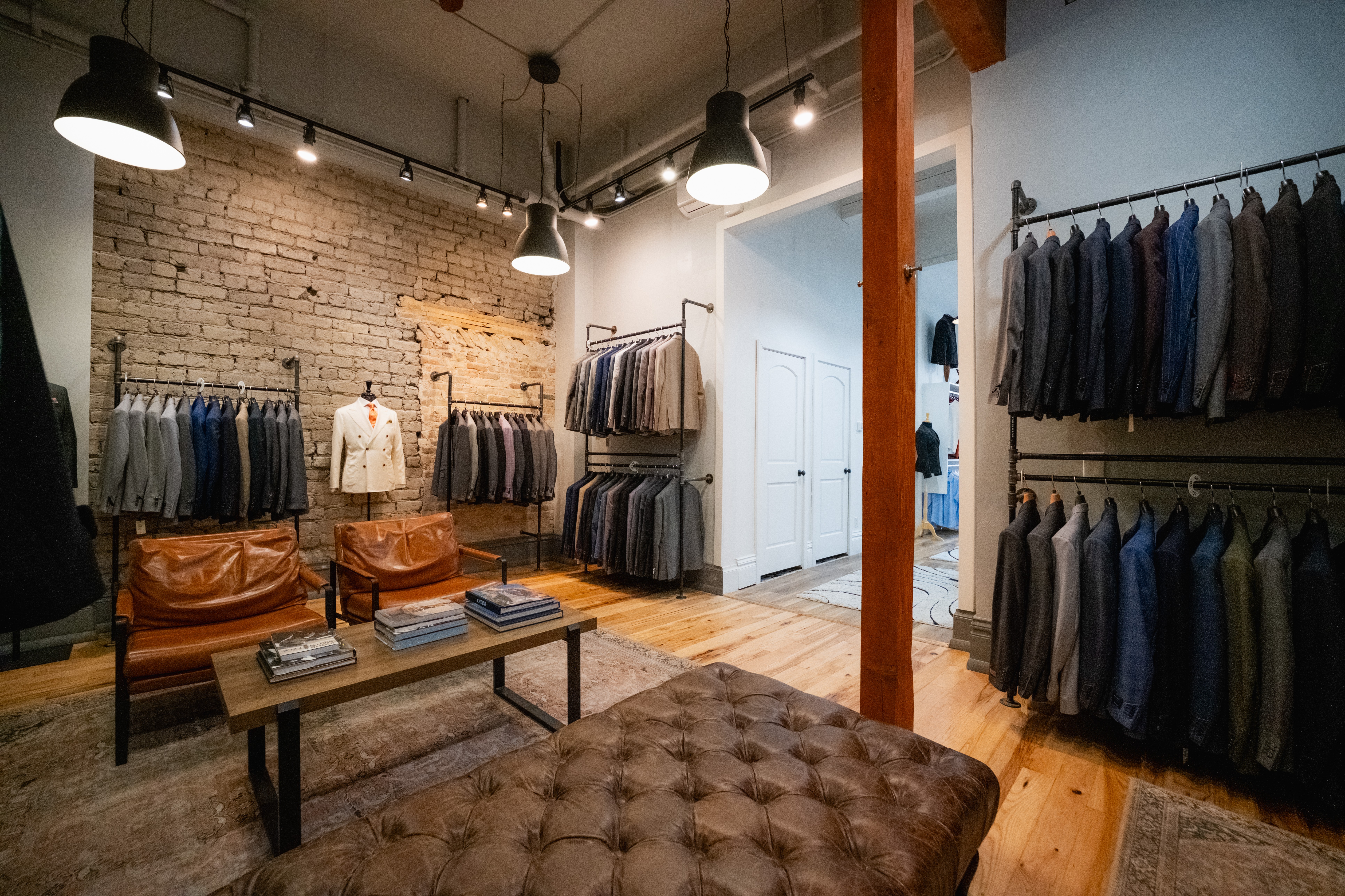 Clothing store interior with racks of jeans, a brick wall, and a wooden floor, illuminated by ceiling lights.