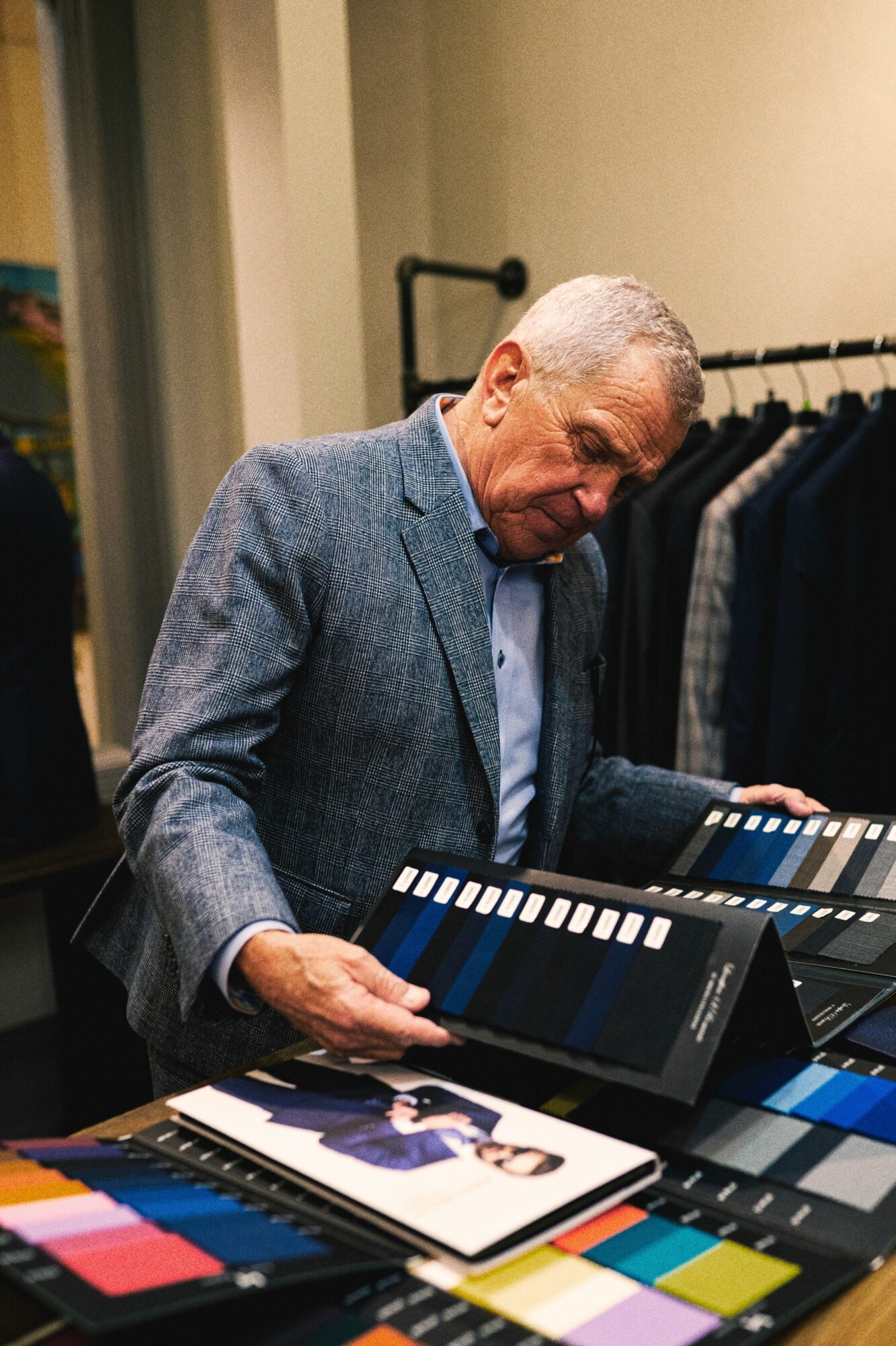 Elderly man in a gray blazer looks at fabric samples in a clothing store.