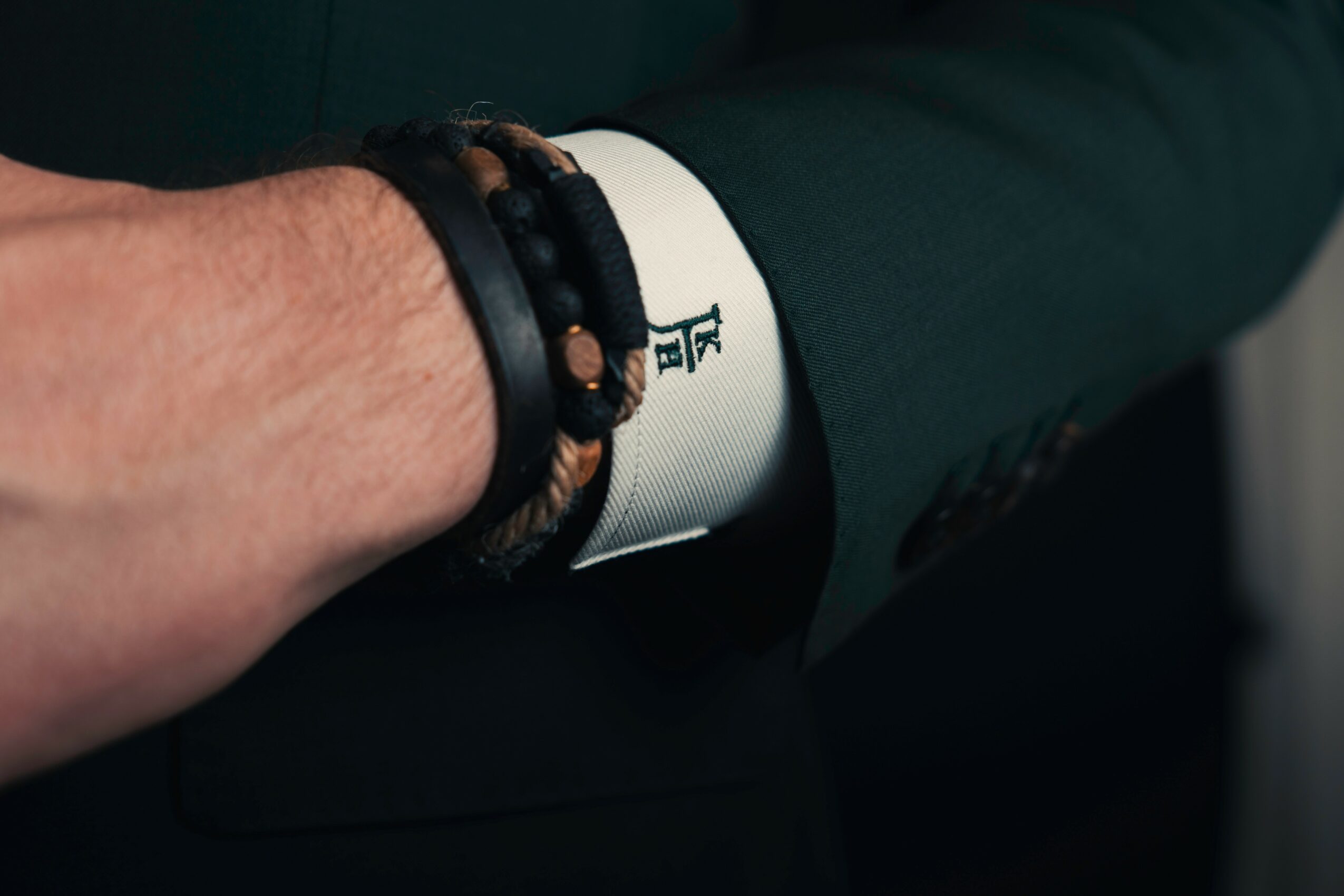 Close-up of a person's arm with bracelets, wearing a suit with a white shirt cuff showing, resting on their lap.