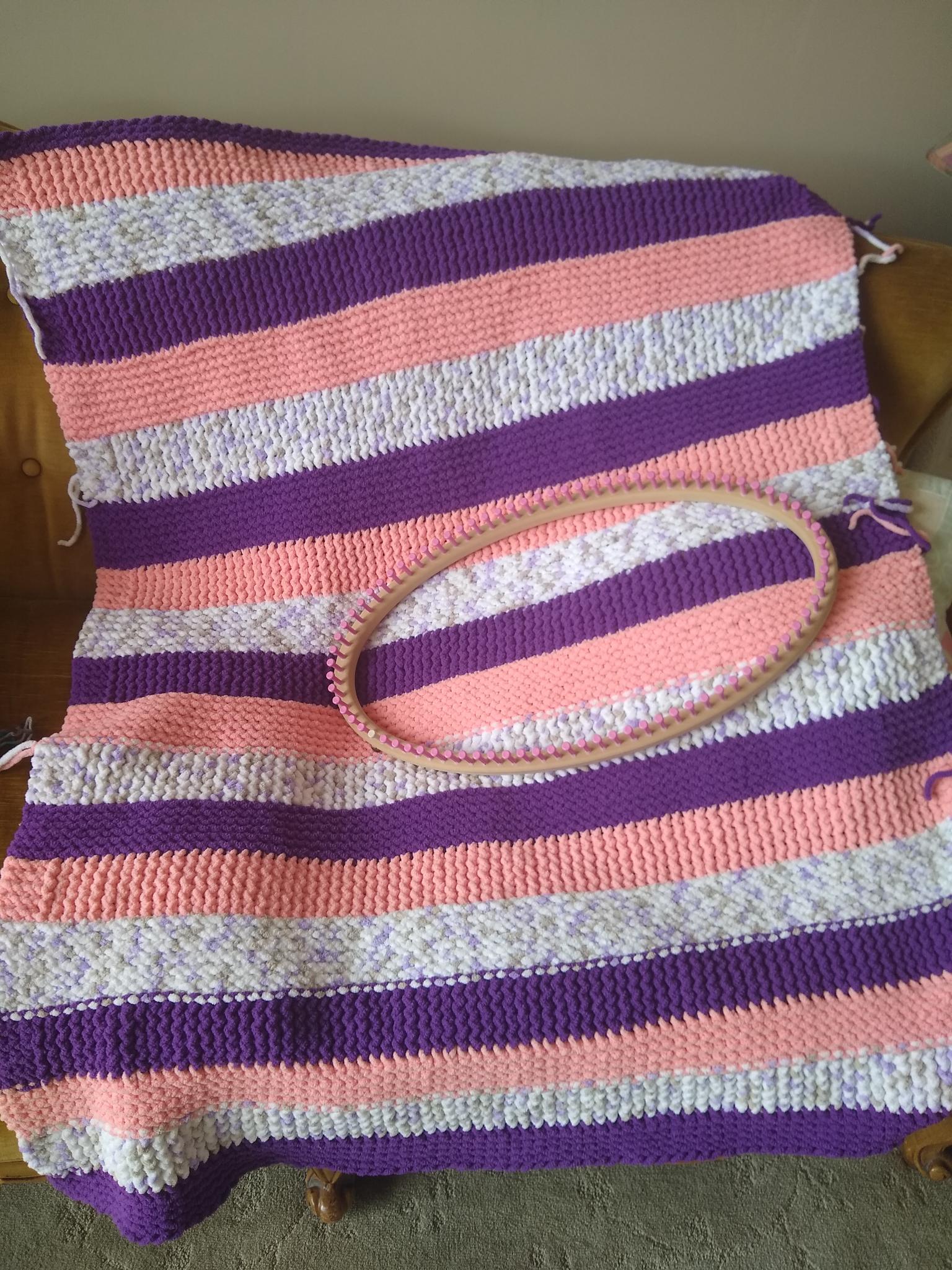 Colorful striped knitted blanket with purple, pink, and white stripes draped over a chair, with a matching necklace on top.