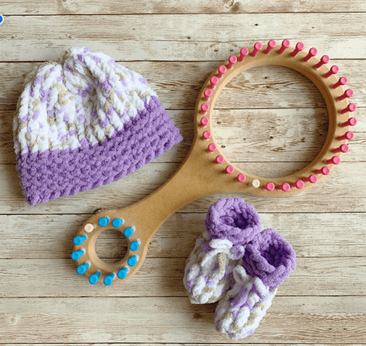 Knitted hat, wooden ring with pink and blue pegs, and purple and white socks on wooden surface.