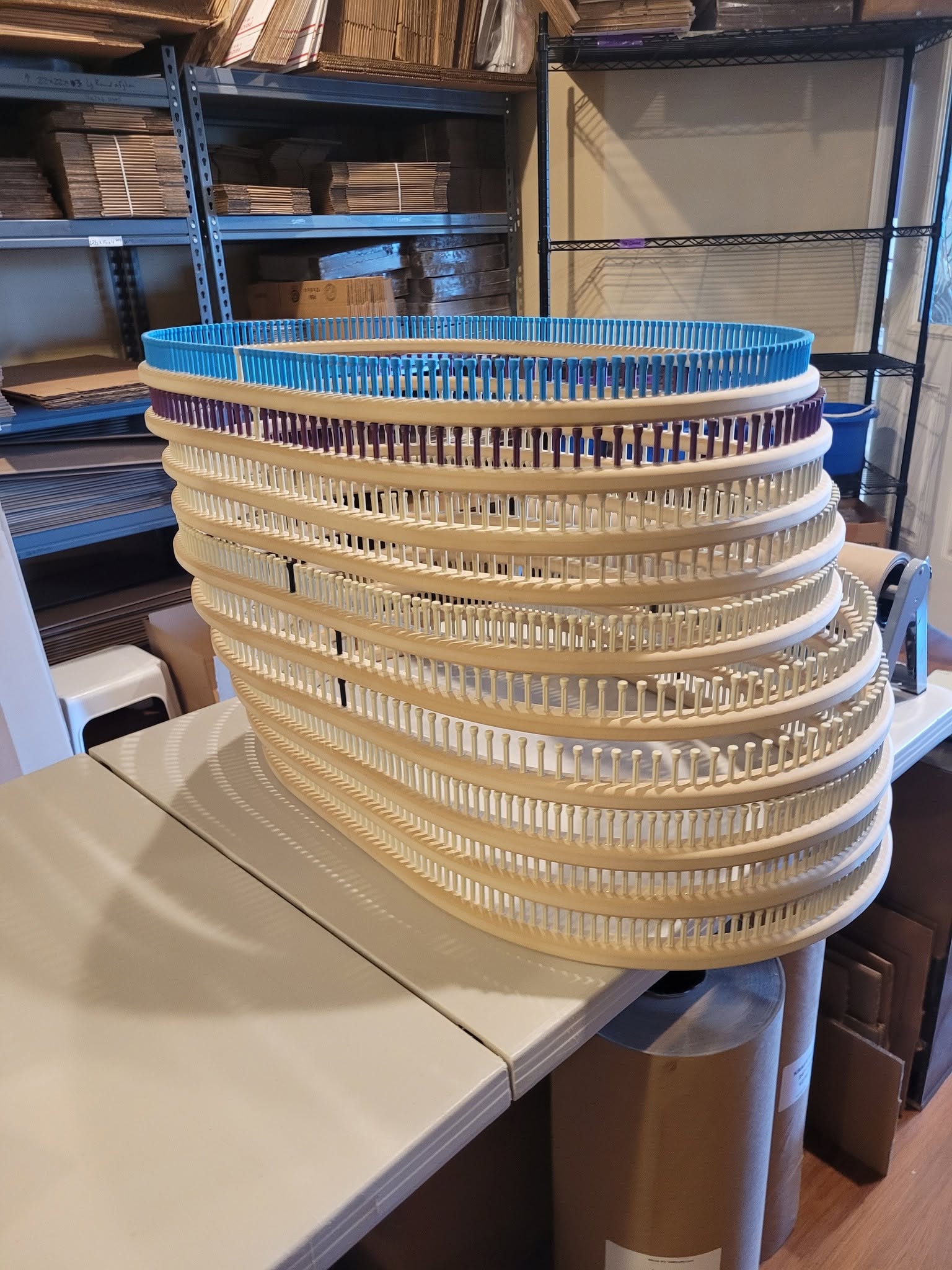 Stacked plastic baskets on a table in a storage room with shelves and boxes in the background.