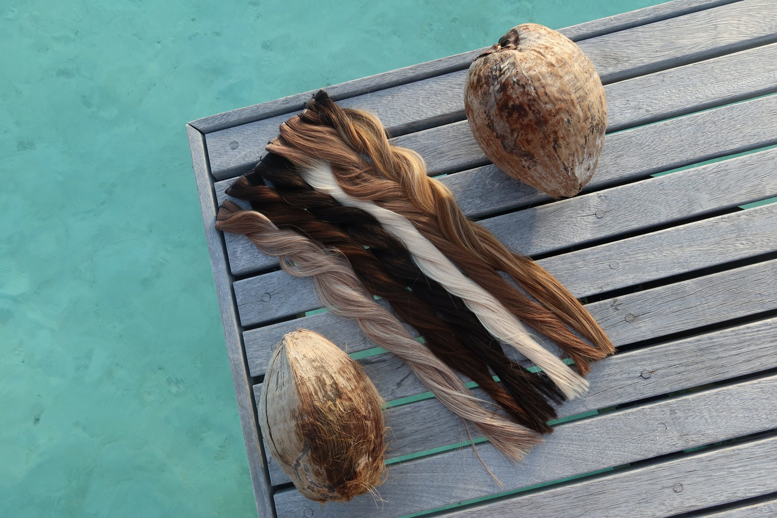 Two coconuts and a bundle of feathers on a wooden dock over water, viewed from above.