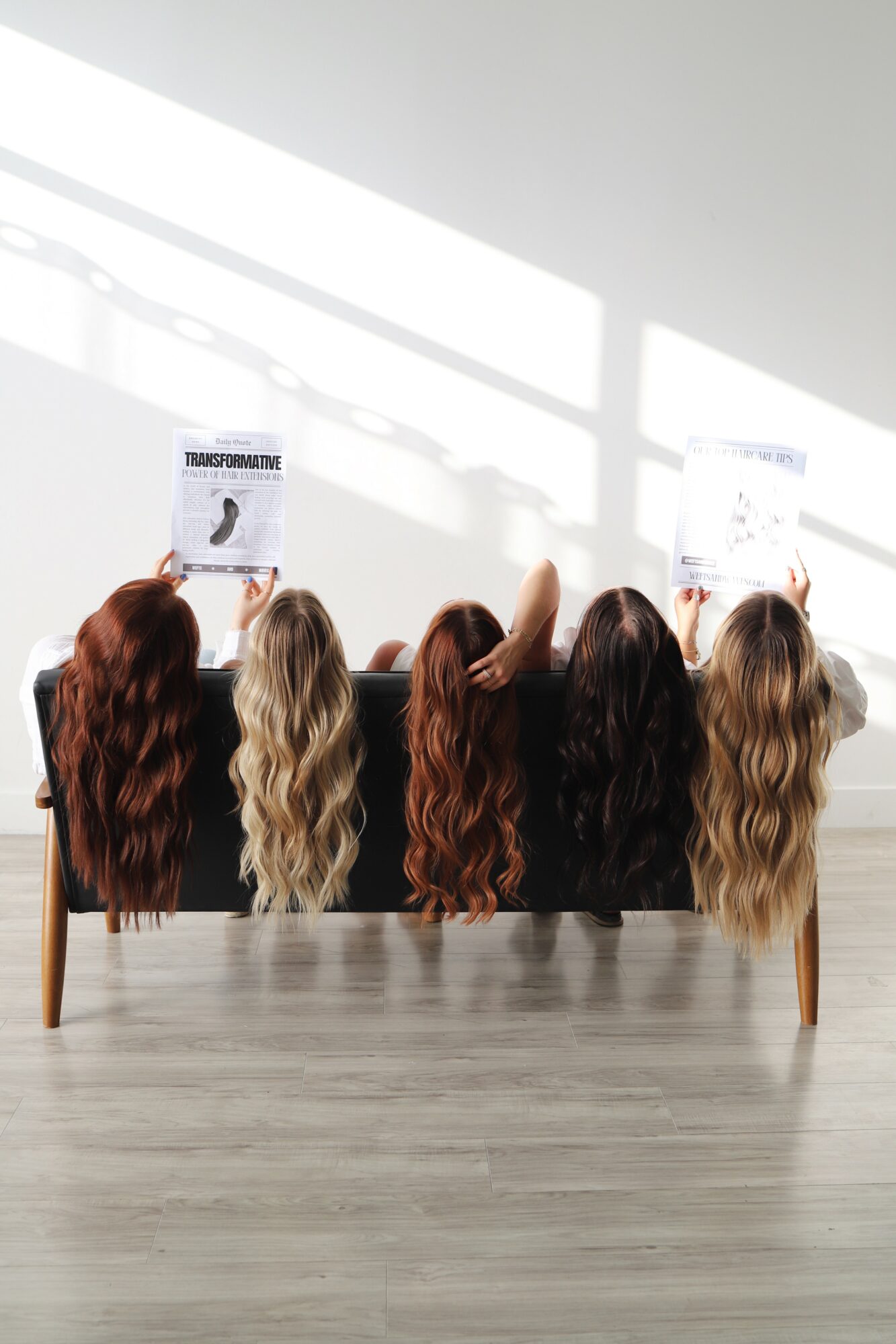 Six mannequin heads with long hair in various shades, displayed on a table against a bright wall with shadows, some holding signs.
