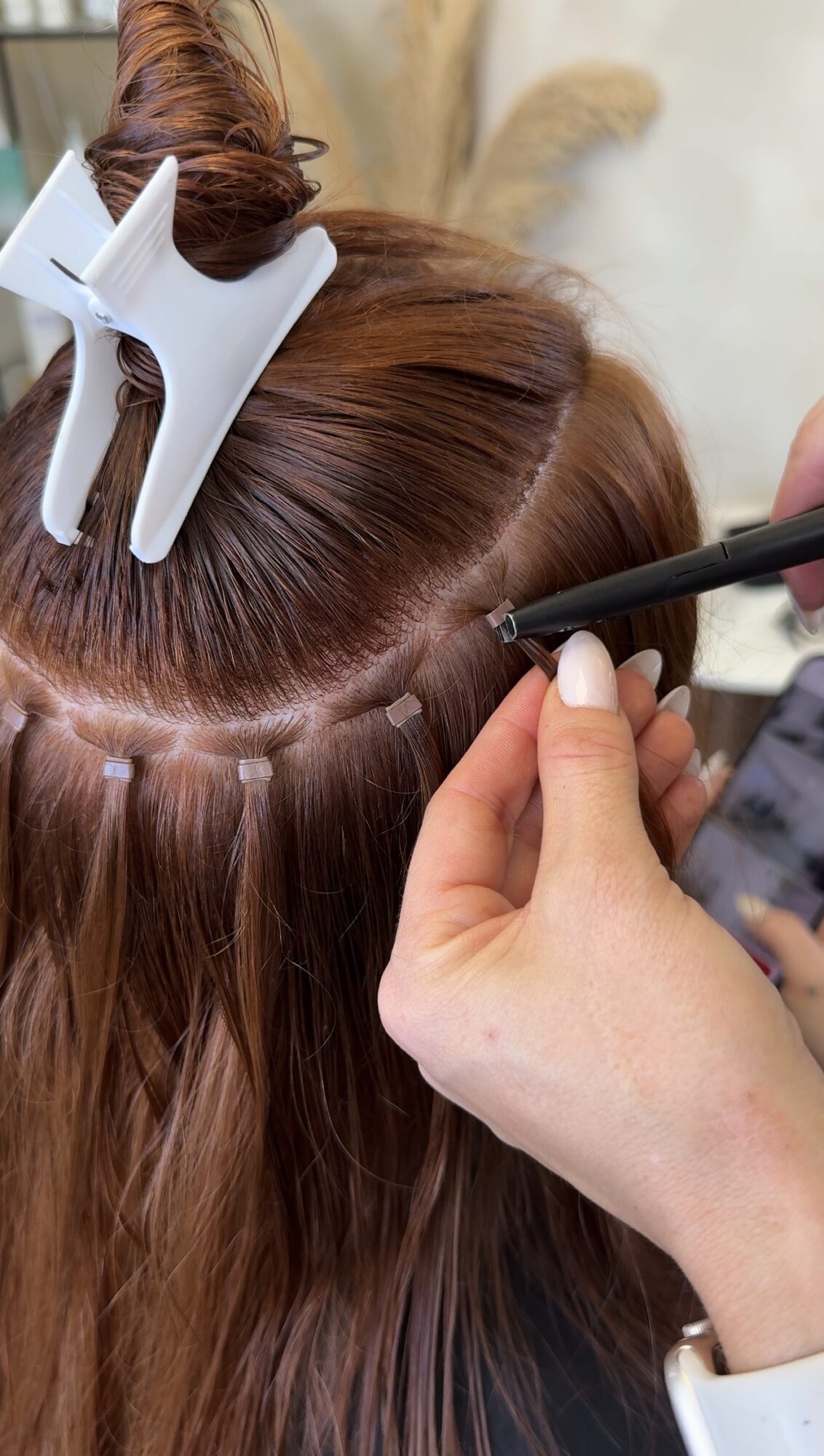 Person applying makeup or eyeliner to a person's hair with a brush, hair held with clips, close-up view.