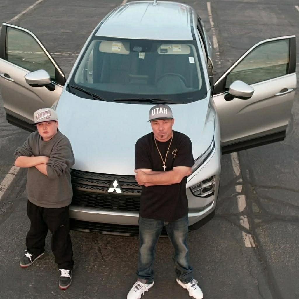 Two young men standing in front of a silver SUV with open doors in a parking lot.