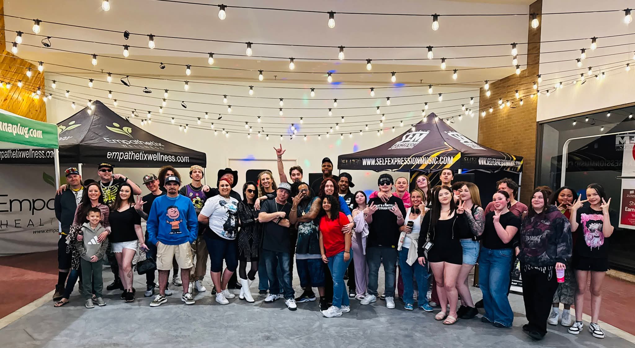 Group of people gathered outdoors under string lights, standing in front of tents, smiling and posing for a photo.