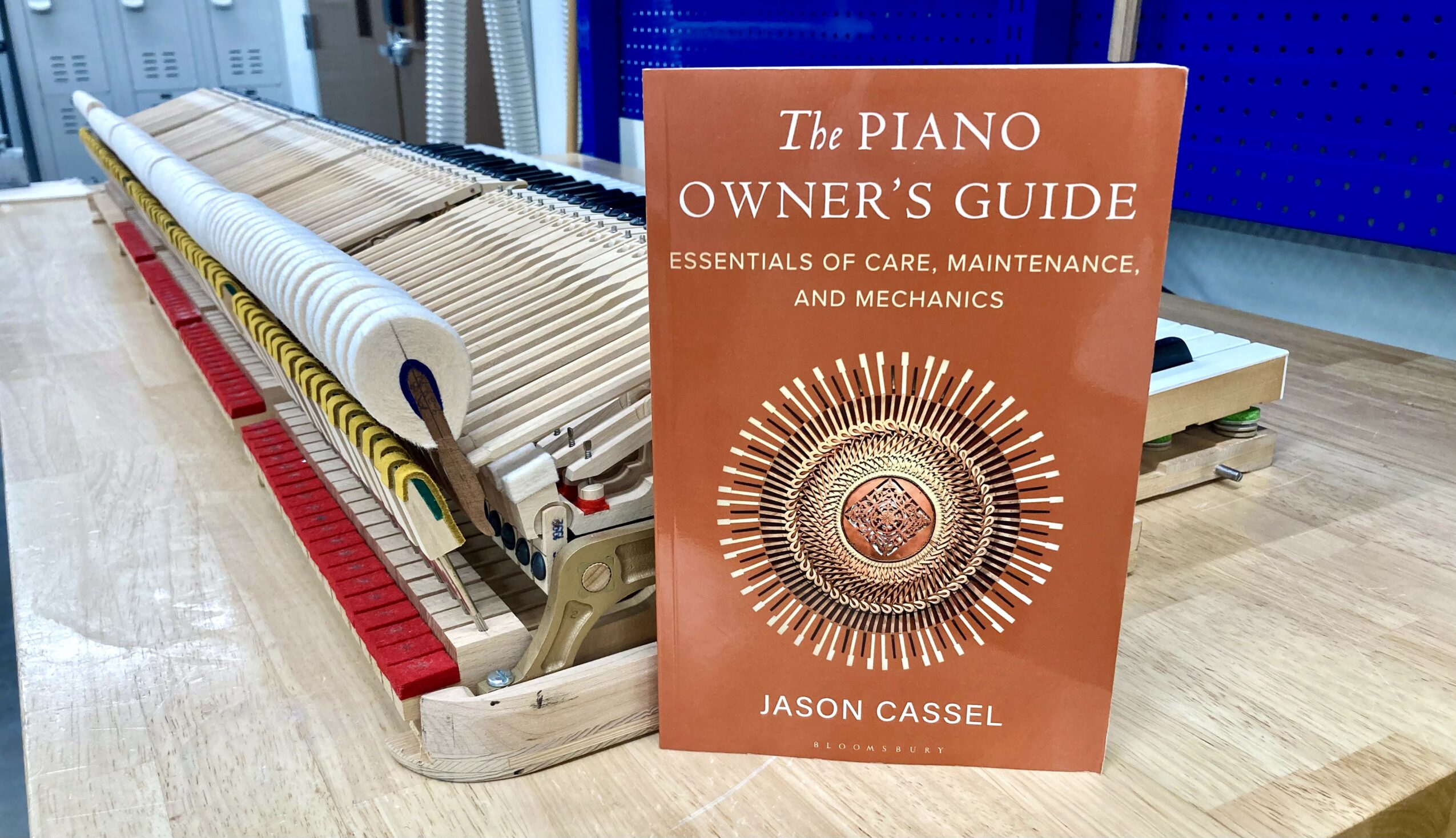 Upright piano with open lid and a book titled 'The Piano Owner's Guide' in front of it, on a wooden floor.
