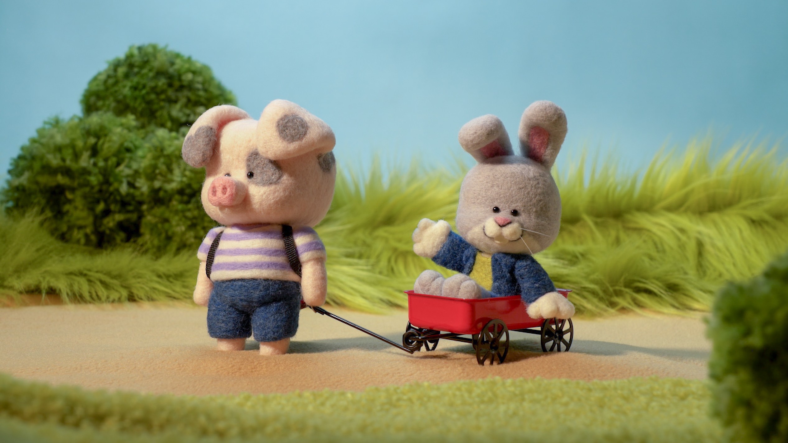 Two plush animal characters, a pig and a rabbit, outdoors with grass and trees, one pulling a red wagon.