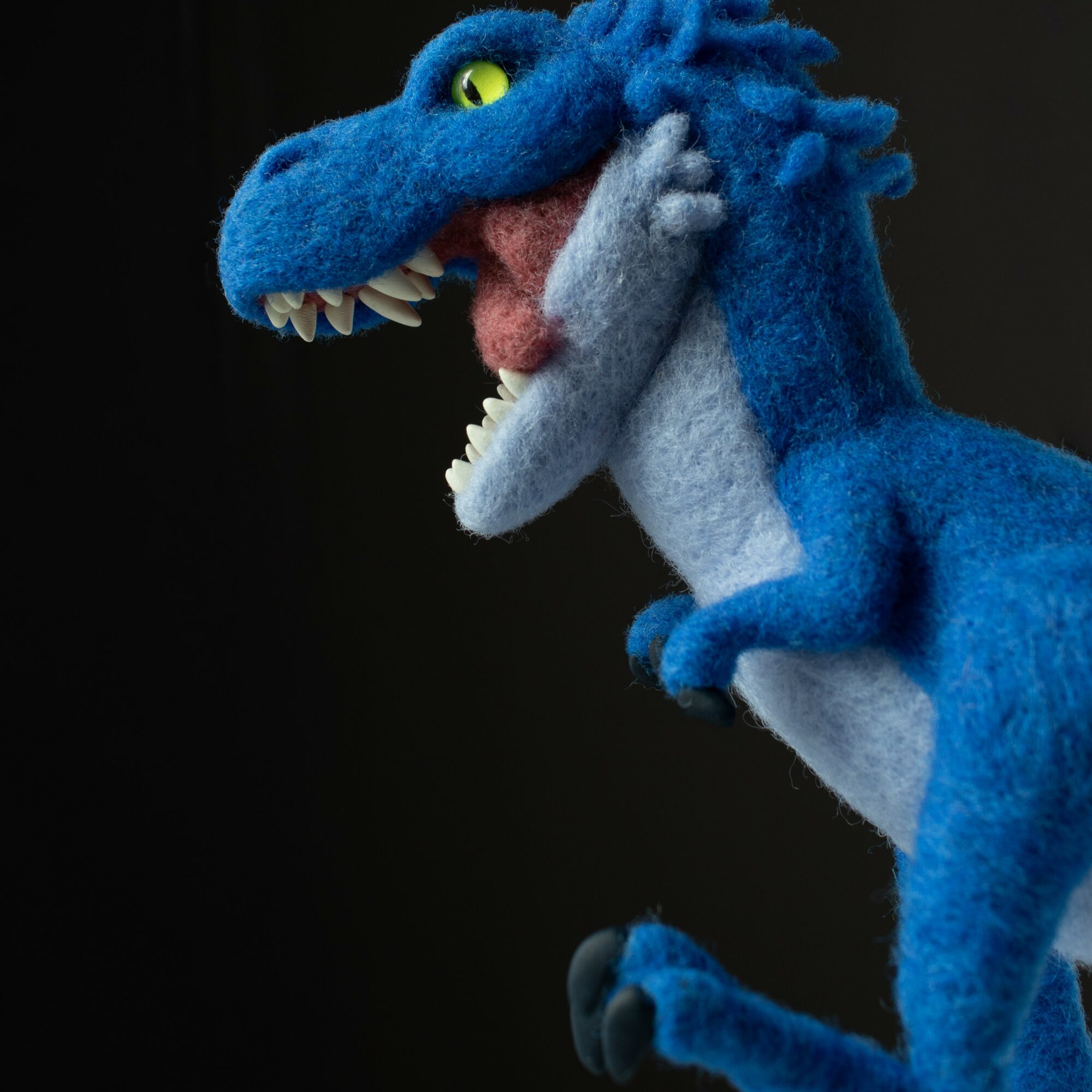 Blue dinosaur puppet with yellow eye and open mouth showing teeth, against a black background.