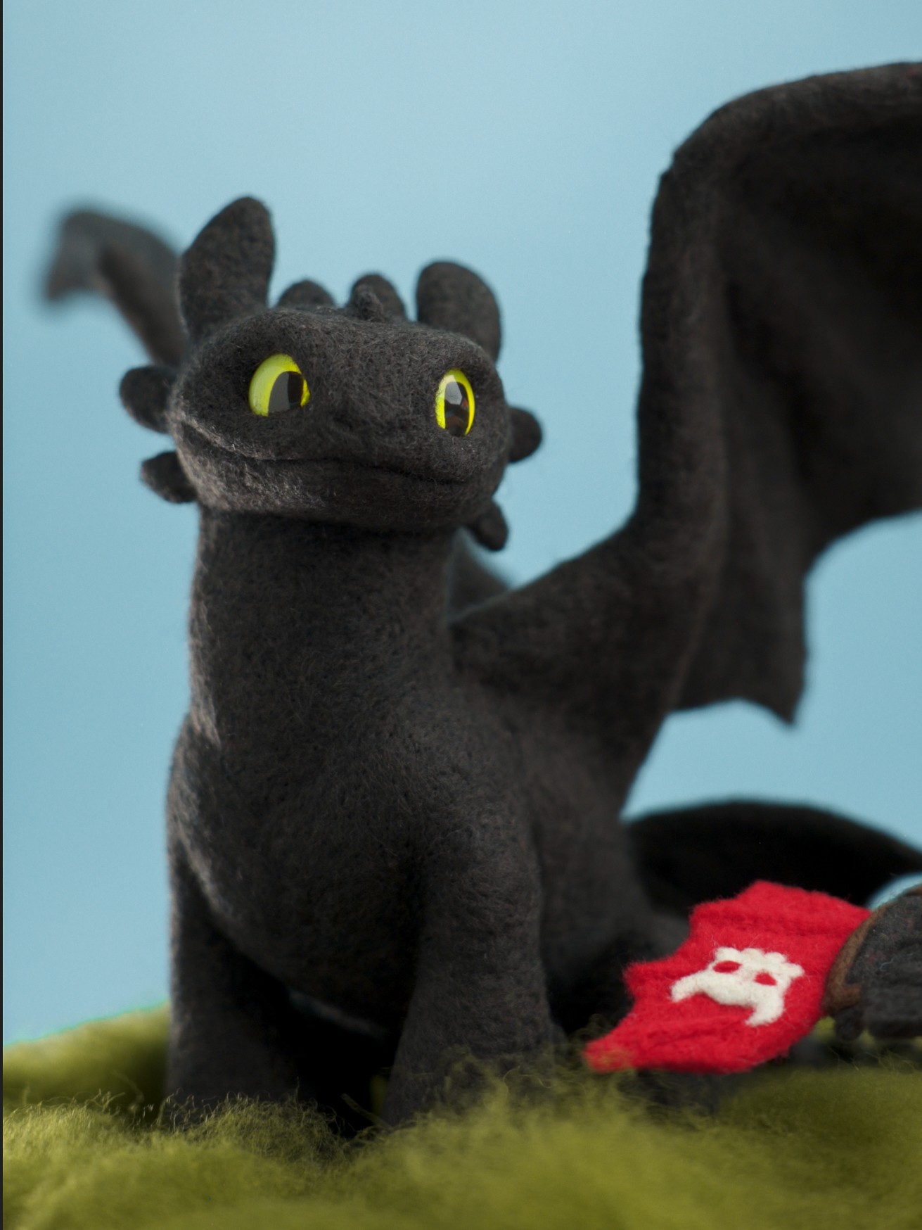 Black plush dragon with yellow eyes, standing on green surface, with a red object nearby, against a blue background.