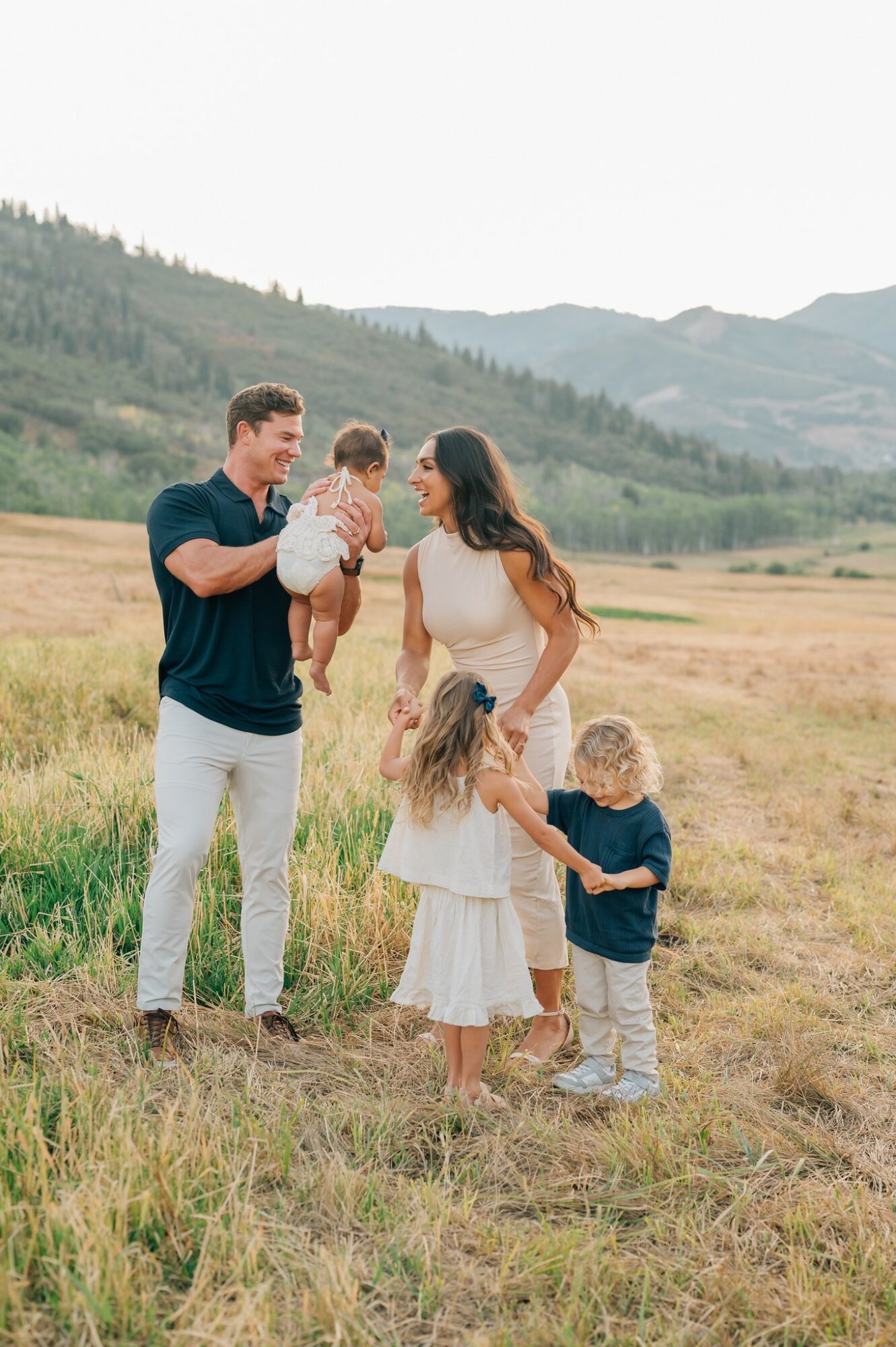 Family of five outdoors in a field with mountains in the background, including a man, woman, and three children.