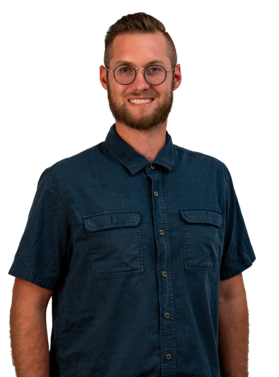Young man with glasses, beard, smiling, wearing a dark blue short-sleeve shirt, standing against a white background.