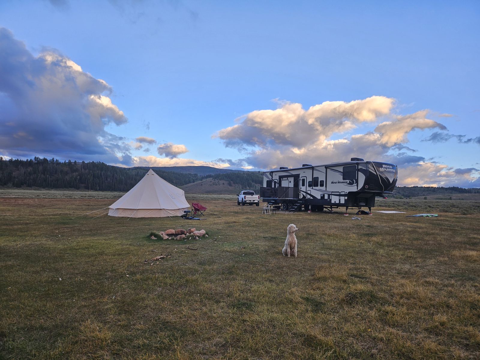 Camping scene with a tent, RV, and a dog on grassy field under blue sky with clouds.