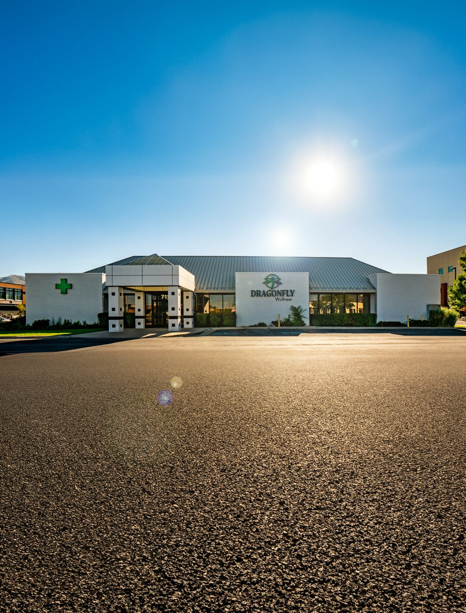 Building with a green cross sign and a sign reading 'DRAGOMY' under a clear blue sky with the sun shining.