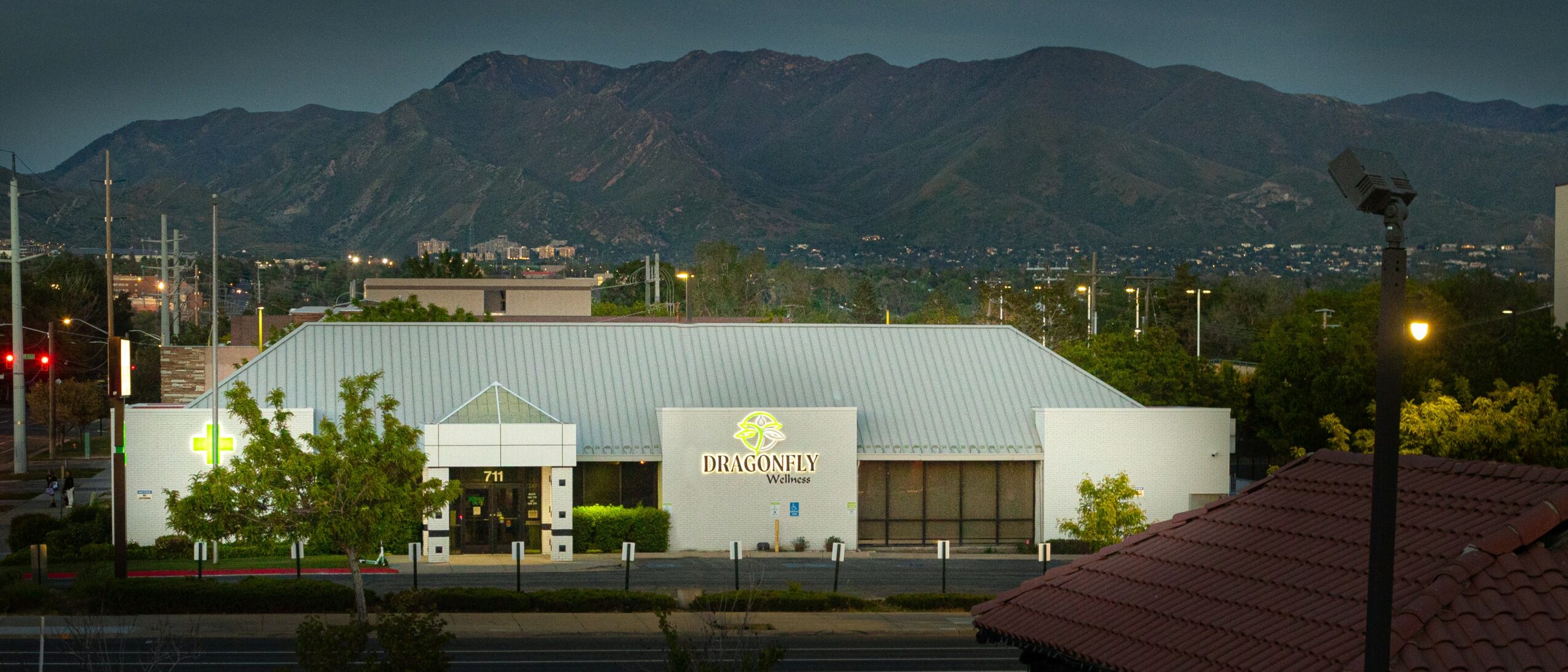 Building with a sign, trees, mountains in the background, and a roof in the foreground.