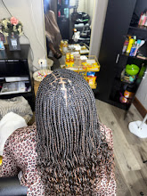 Person with long, curly hair sitting in a salon chair, facing a mirror, with shelves and products in the background.