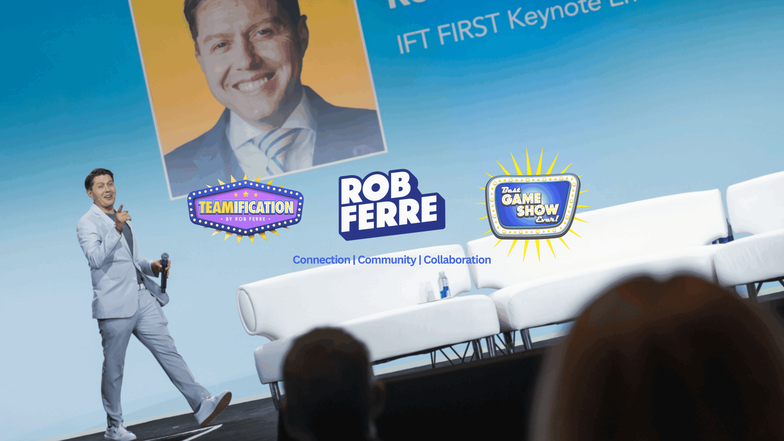 Speaker on stage with a large screen behind him, white chairs on stage, audience in foreground.