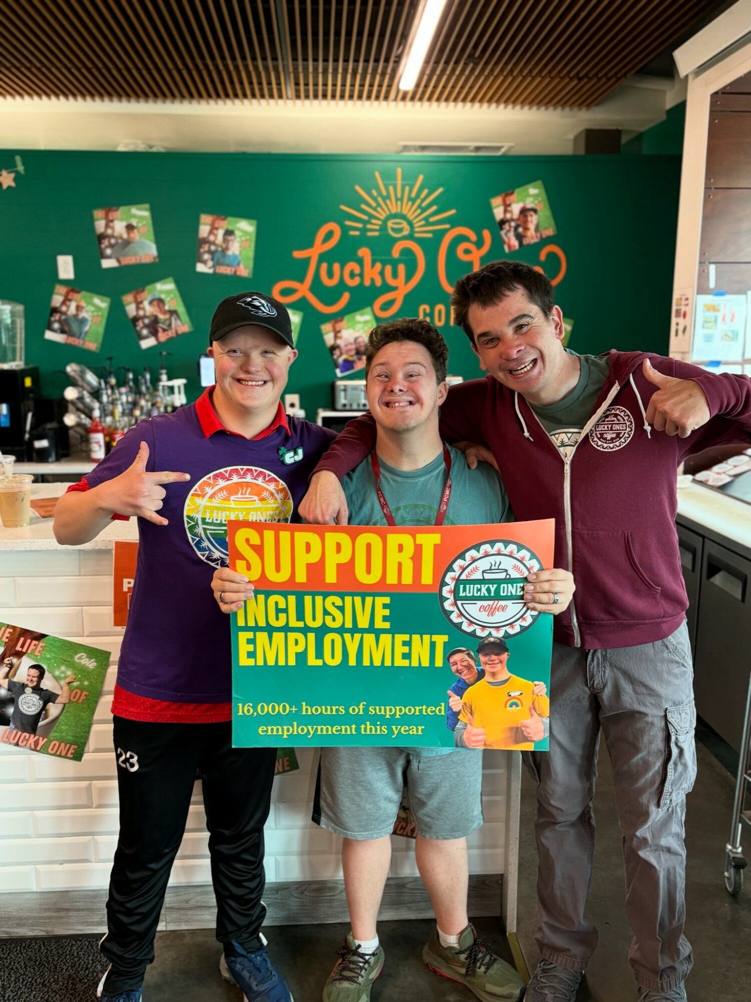 Three smiling people holding a support sign in a colorful indoor setting with a green wall and Lucky Charms branding.