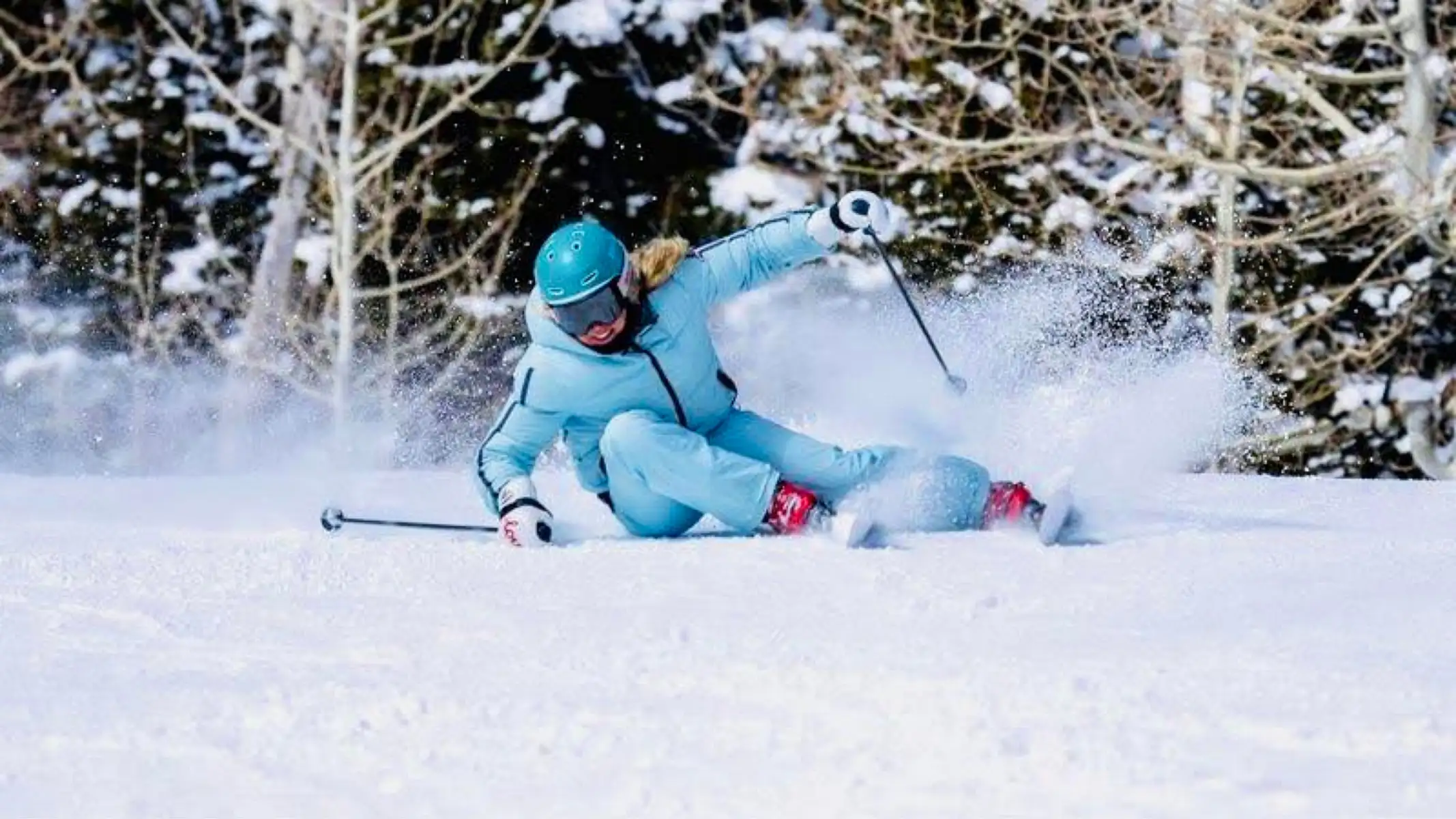 Person skiing downhill on snow, wearing blue gear and helmet, surrounded by snow-covered trees.