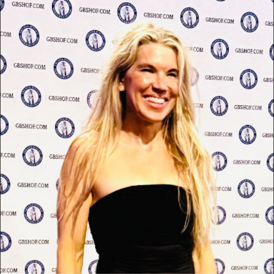 Woman with long blonde hair smiling in front of a backdrop with logos and text.