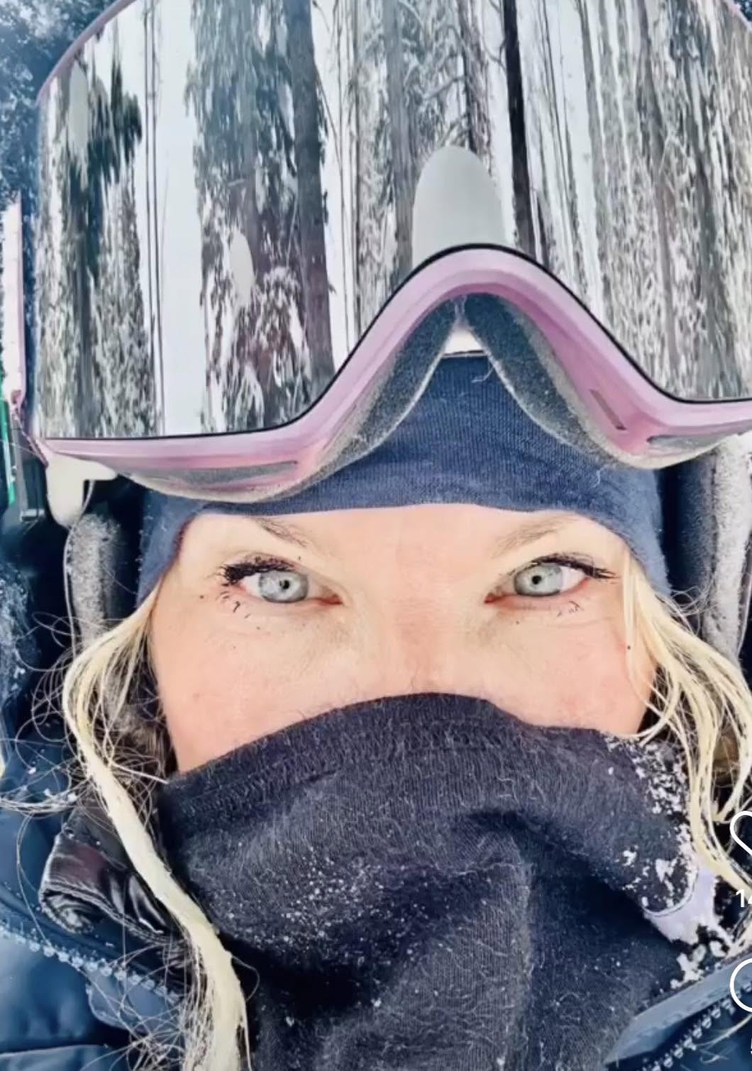 Person wearing ski goggles, a beanie, and a face covering, with snow on the face covering, outdoors in a snowy environment.