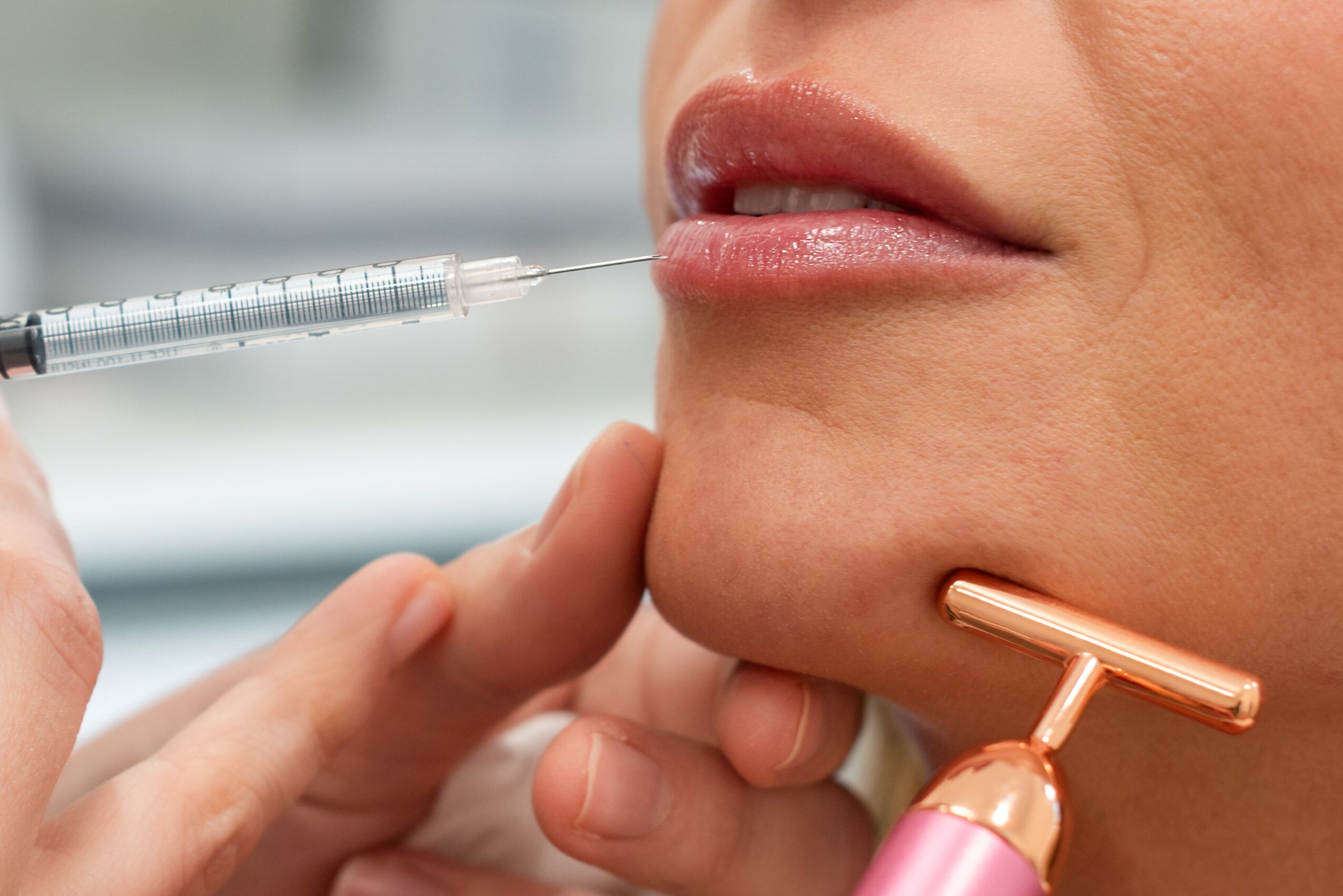 Person receiving a cosmetic injection near the lips, with a skincare tool held against the chin.