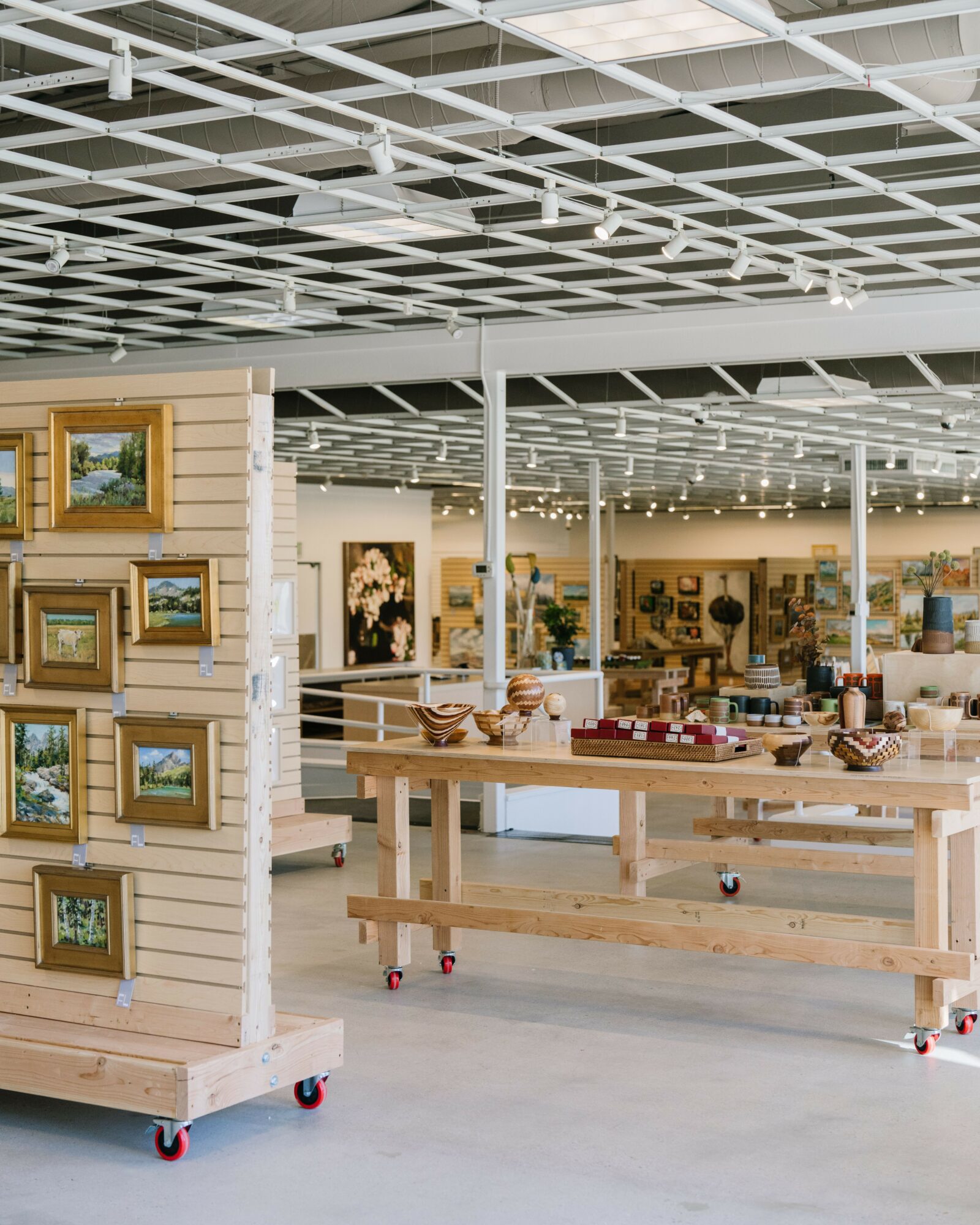 Interior of a store with display tables and artwork, ceiling with grid pattern, and bright lighting.