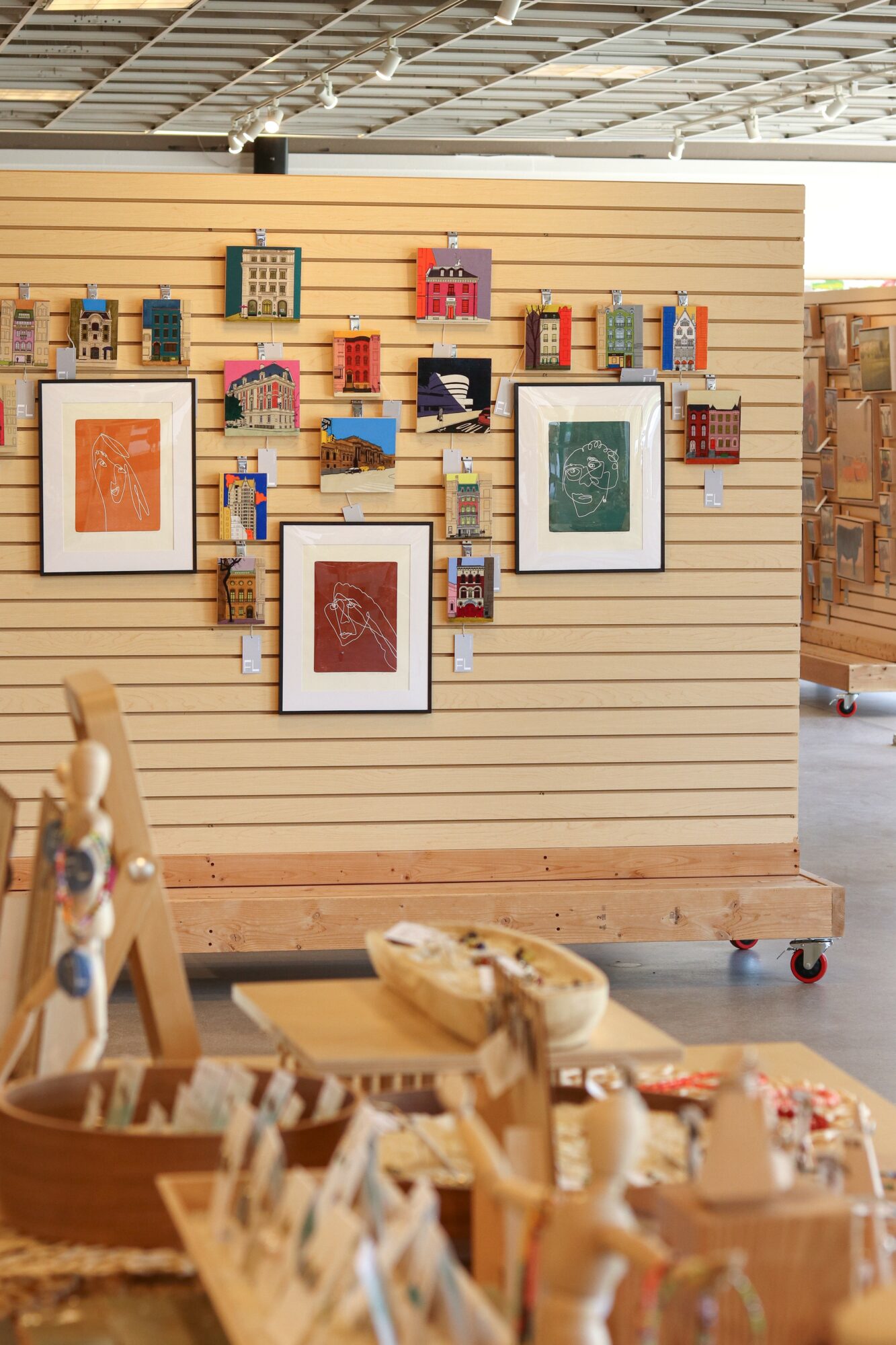 Wooden display wall with framed artwork and small decorative items, in a store setting.