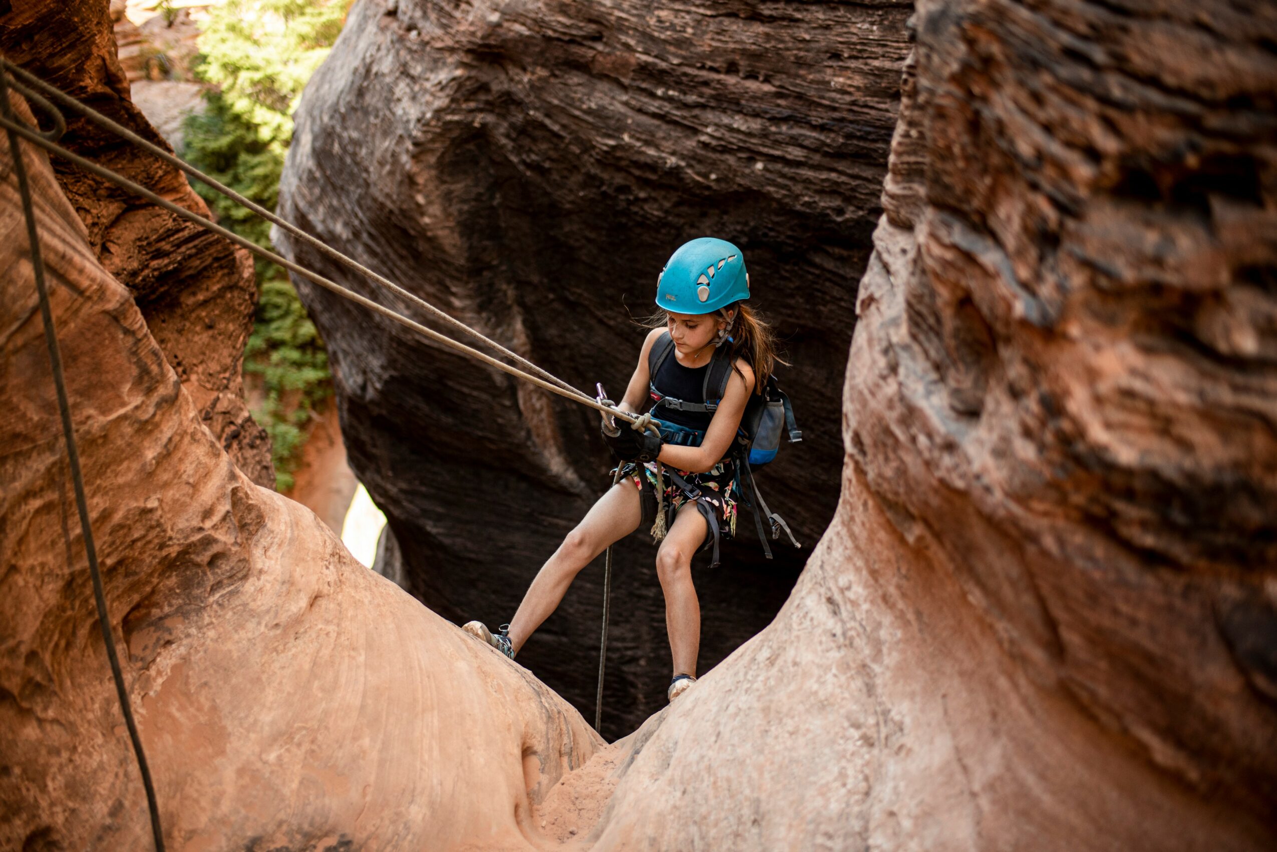 Person wearing a blue helmet and harness, rappelling between rock formations outdoors.
