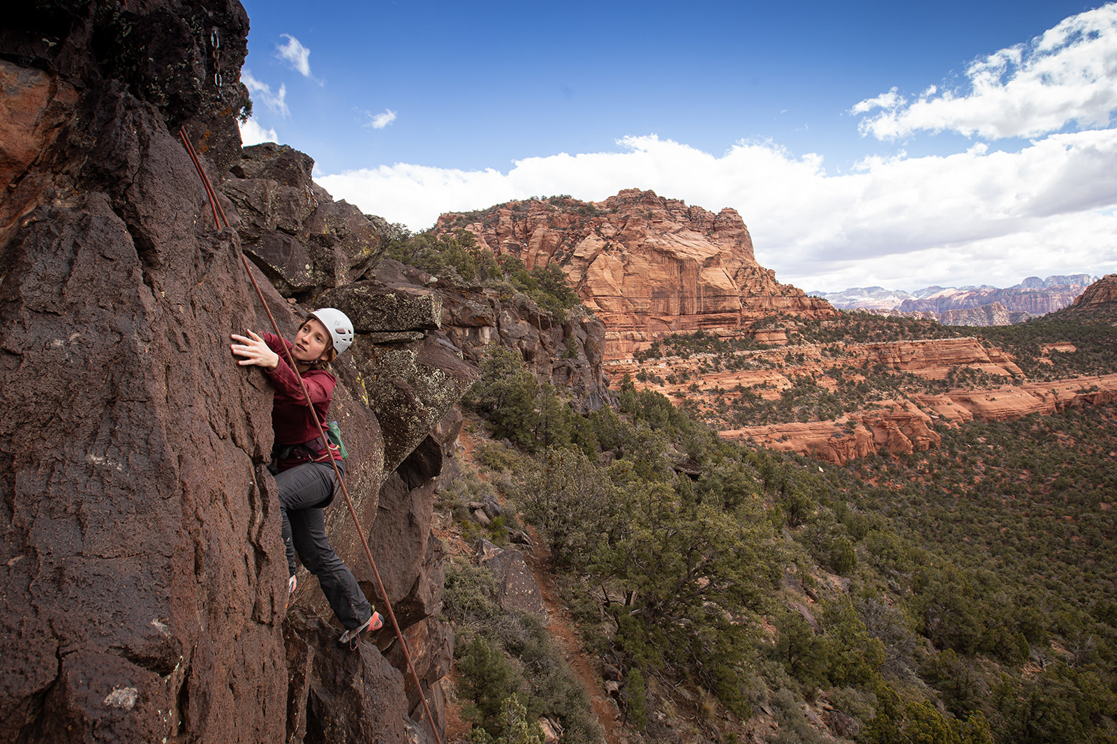 Person climbing a rock face outdoors with a scenic canyon and sky in the background.