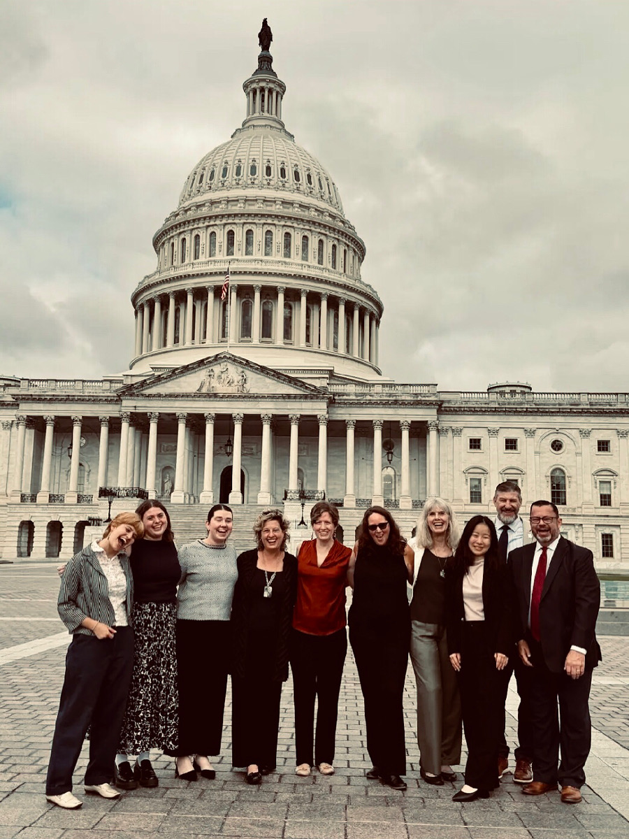 Group of eight people standing in front of the U.S. Capitol building on a cloudy day.