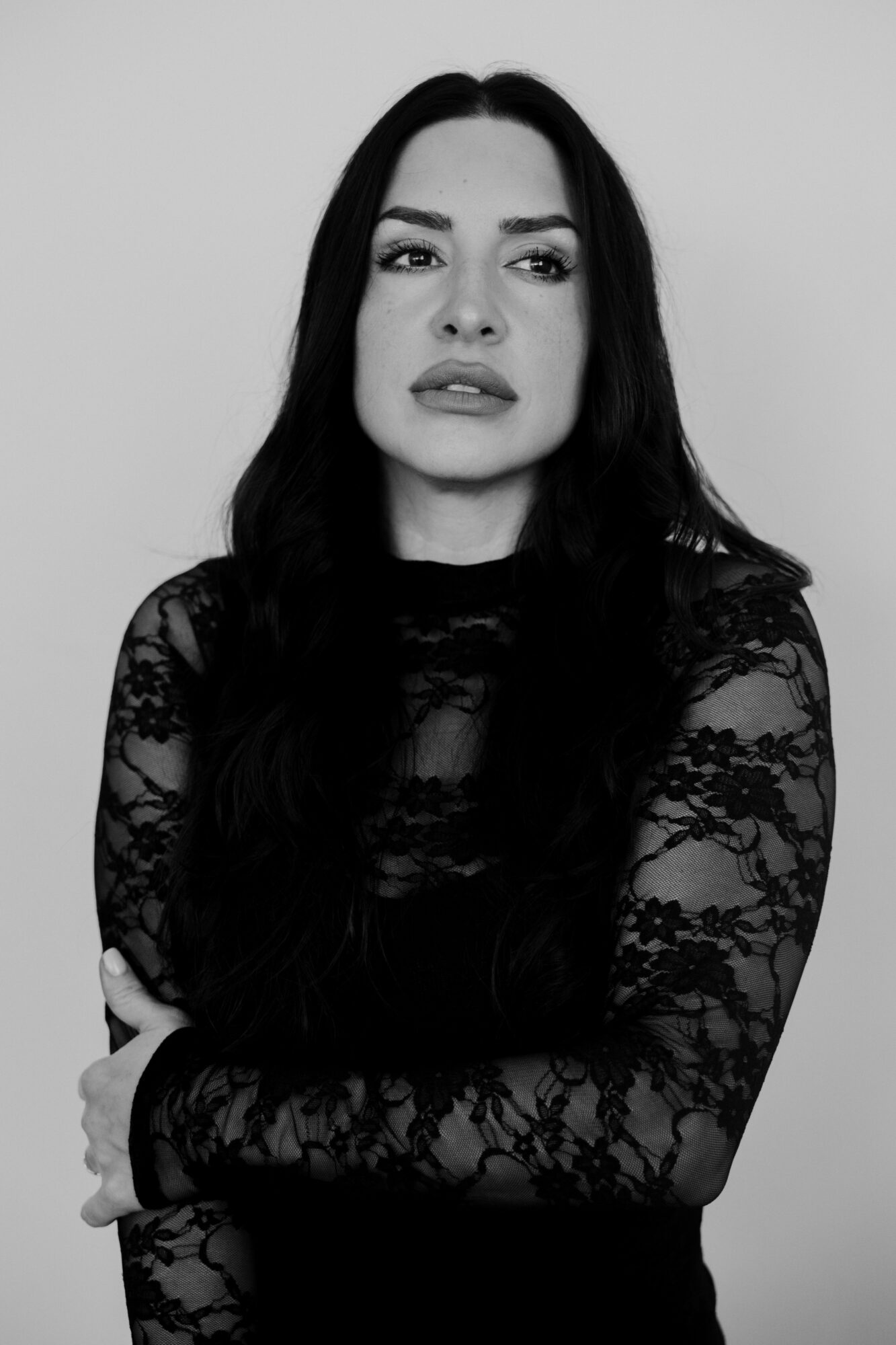 Woman with long dark hair wearing a lace top, looking to the side, in black and white.