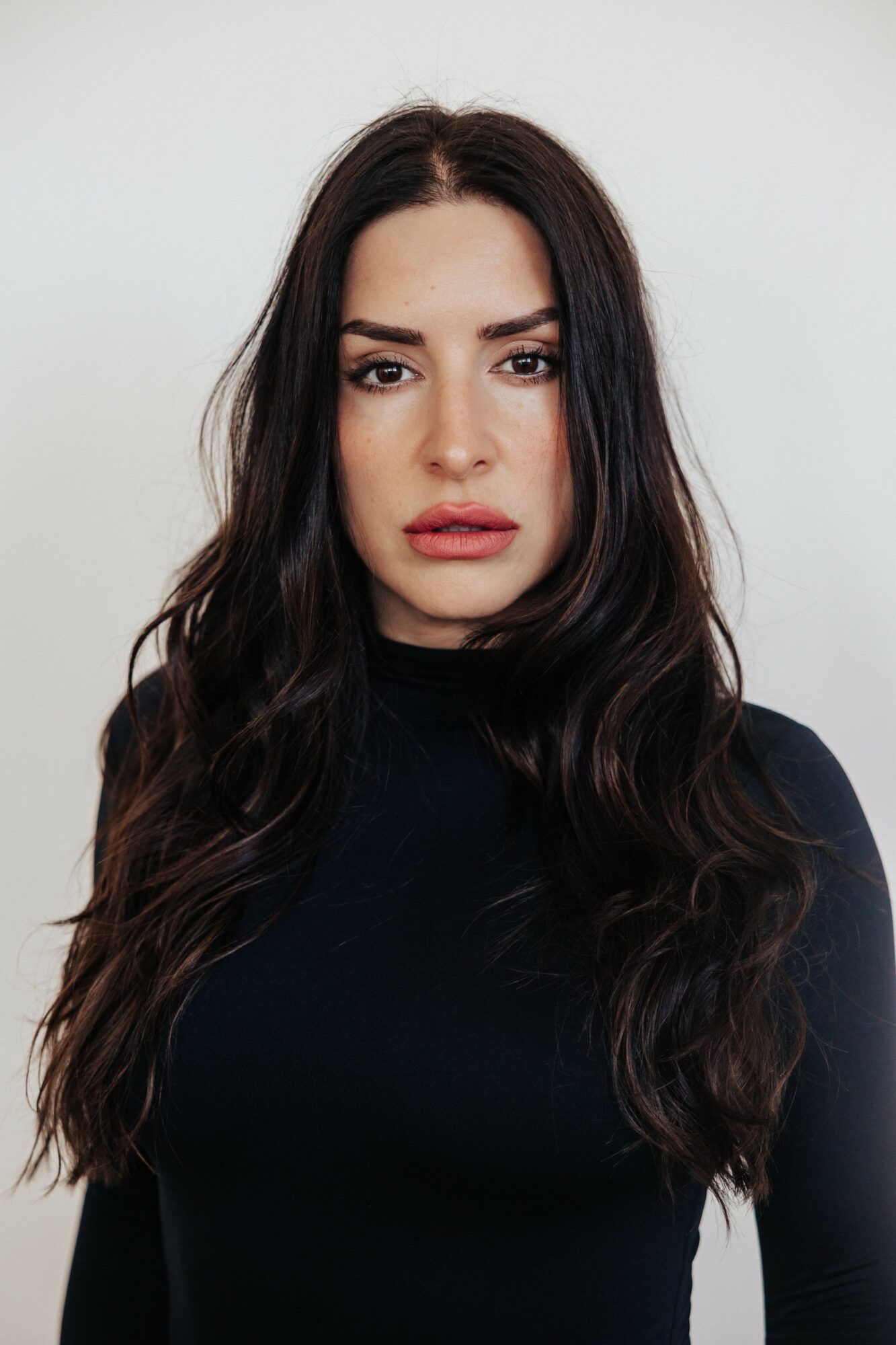 Woman with long dark hair and neutral expression wearing a black top, facing forward against a plain background.