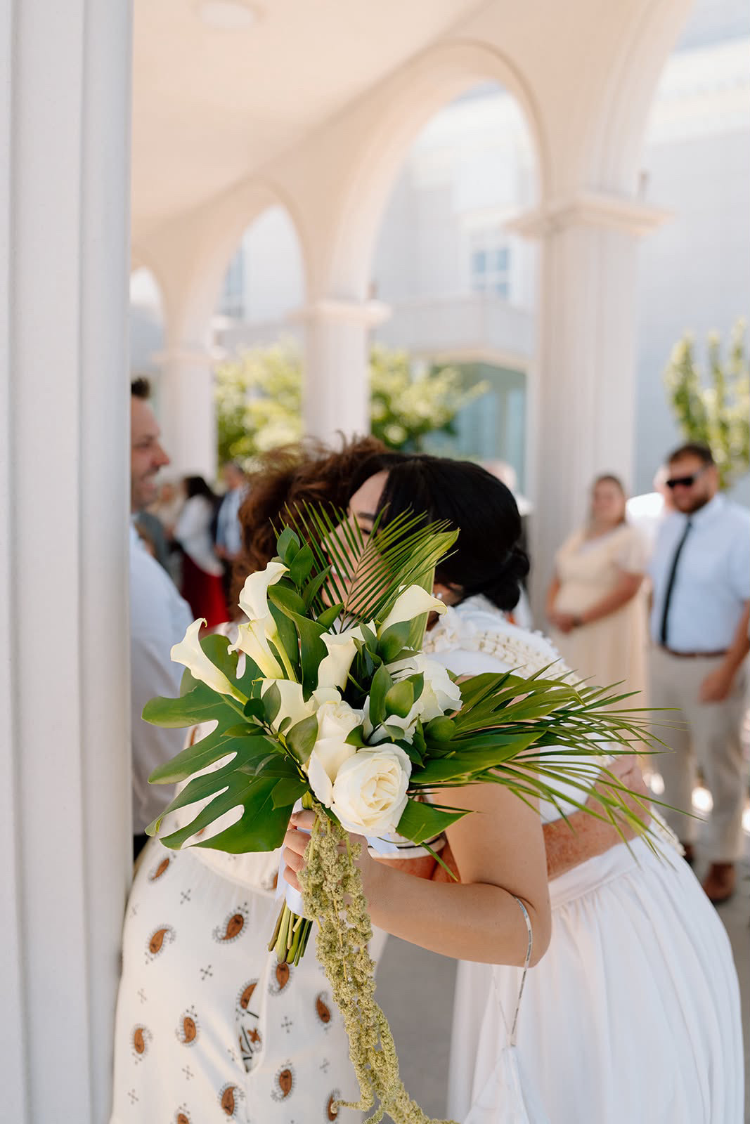 A person in a white dress holds a large bouquet of white flowers and greenery in a bright arched room.
